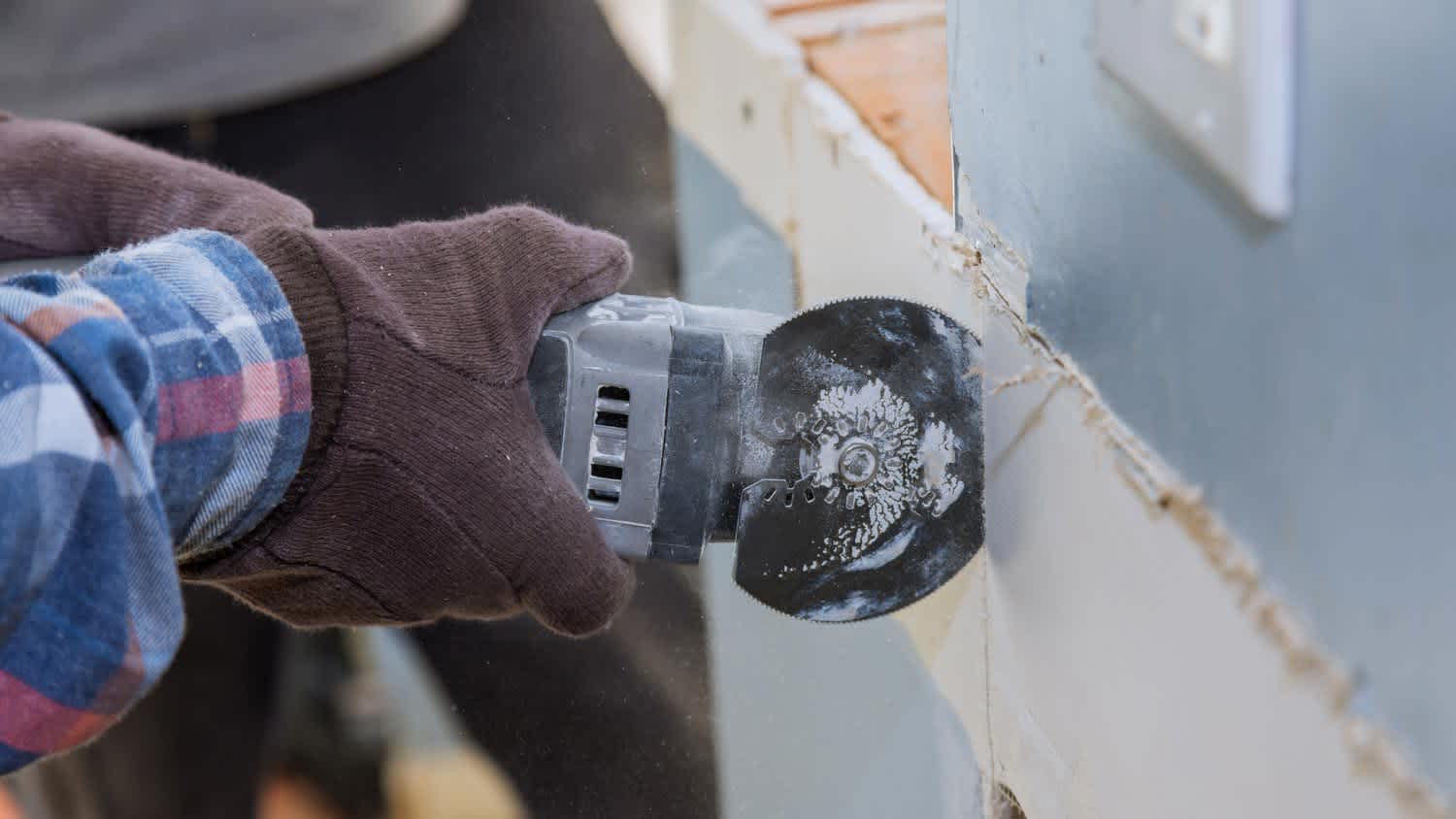 Close-up of a hand cutting a drywall with a saw