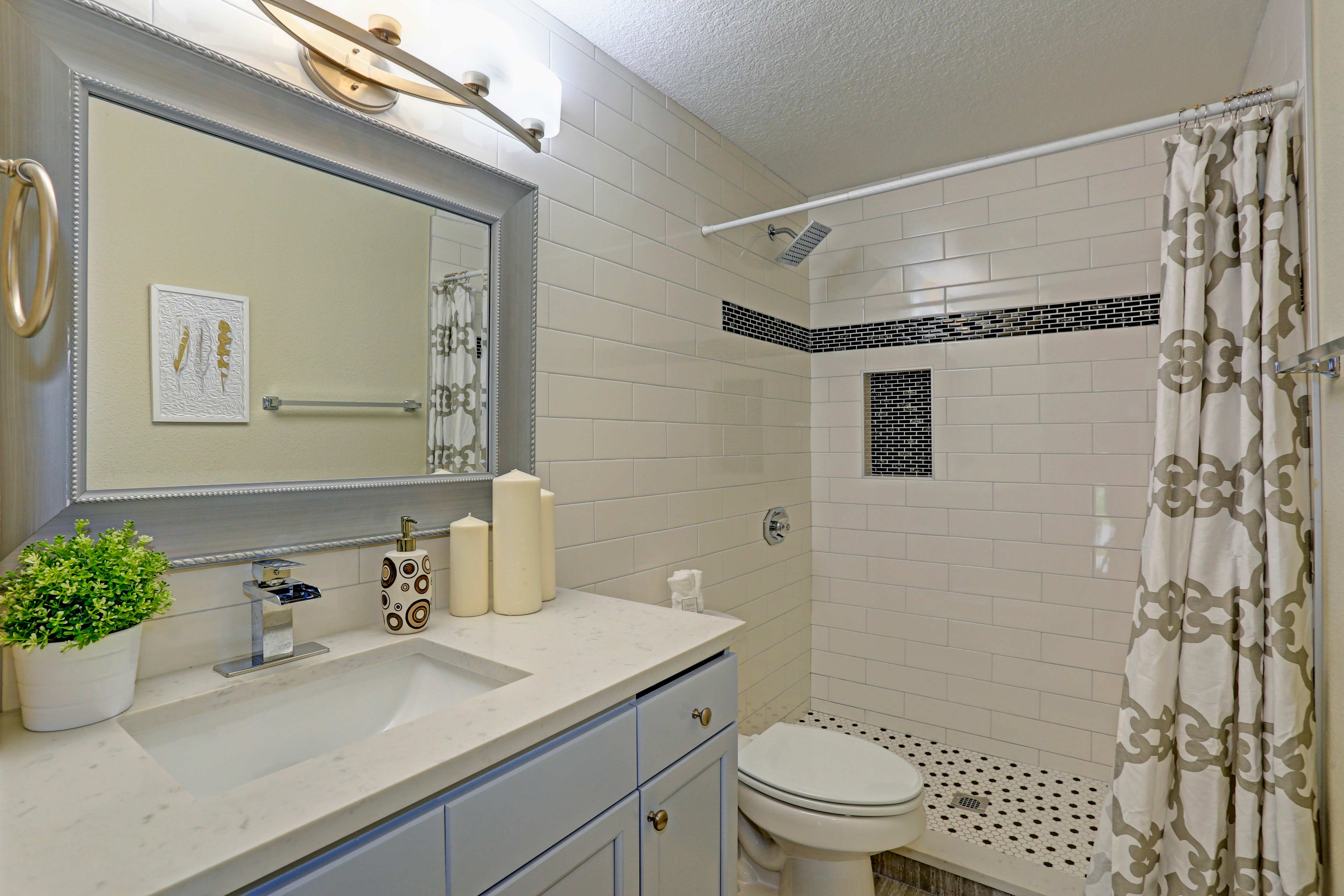 A bathroom with a walk-in shower, gold-and-white shower curtain, and gold accents