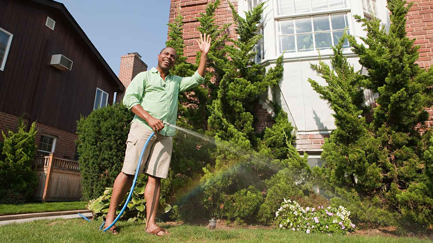 Man watering plants with a hose and waving the neighbors