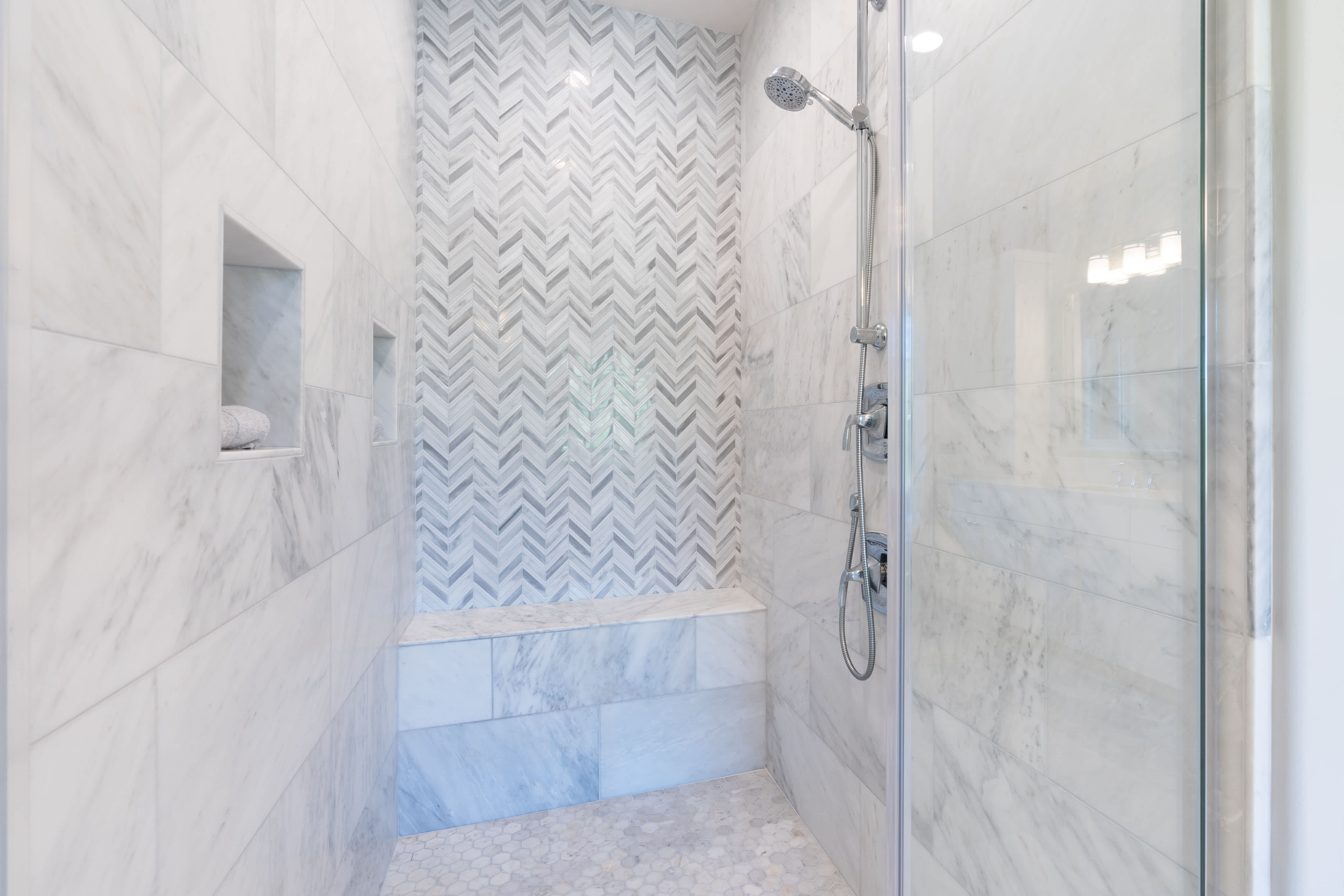 A walk-in shower with marble tile and a contrasting herringbone pattern