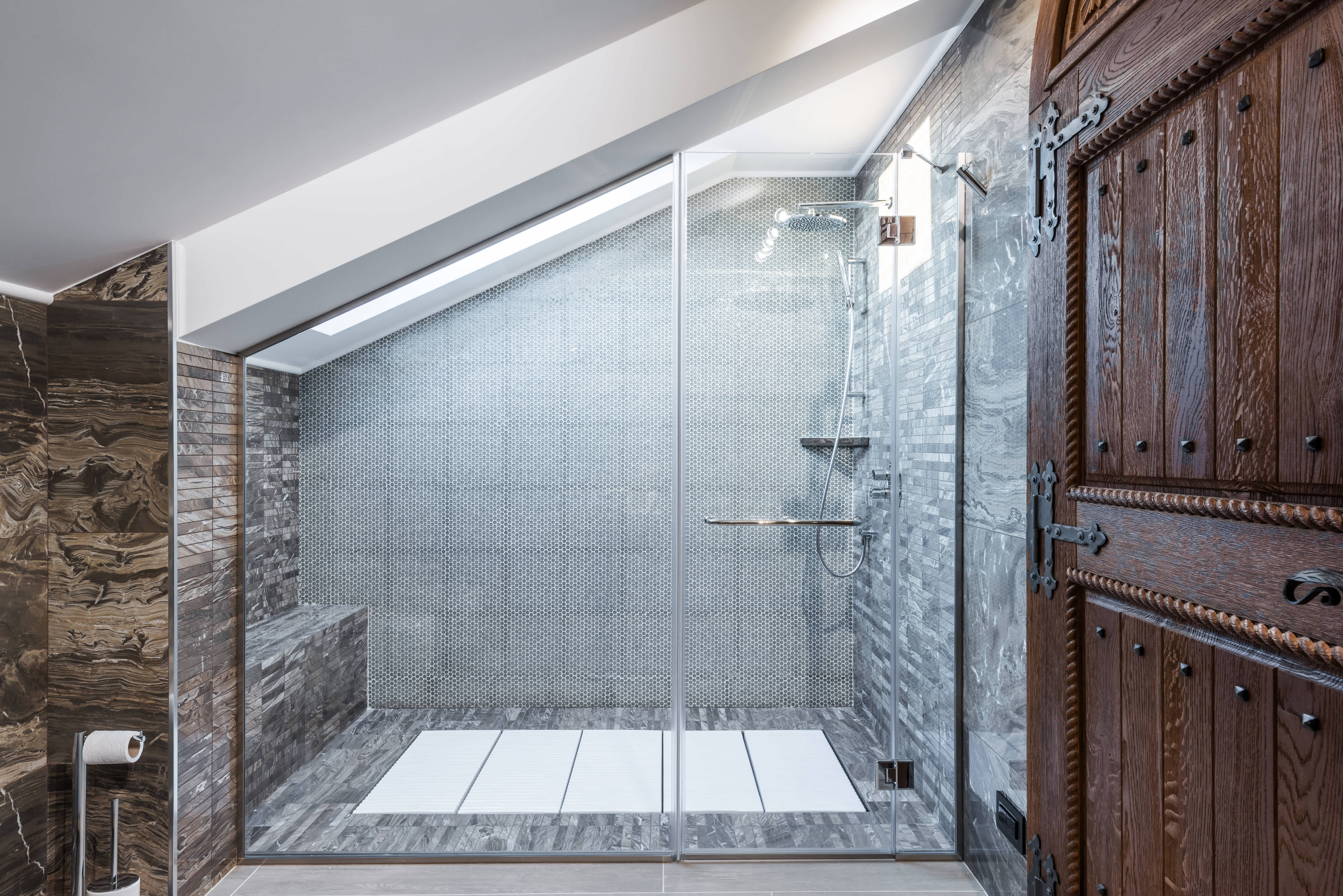 A walk-in shower with a skylight and a mix of mosaic tiles