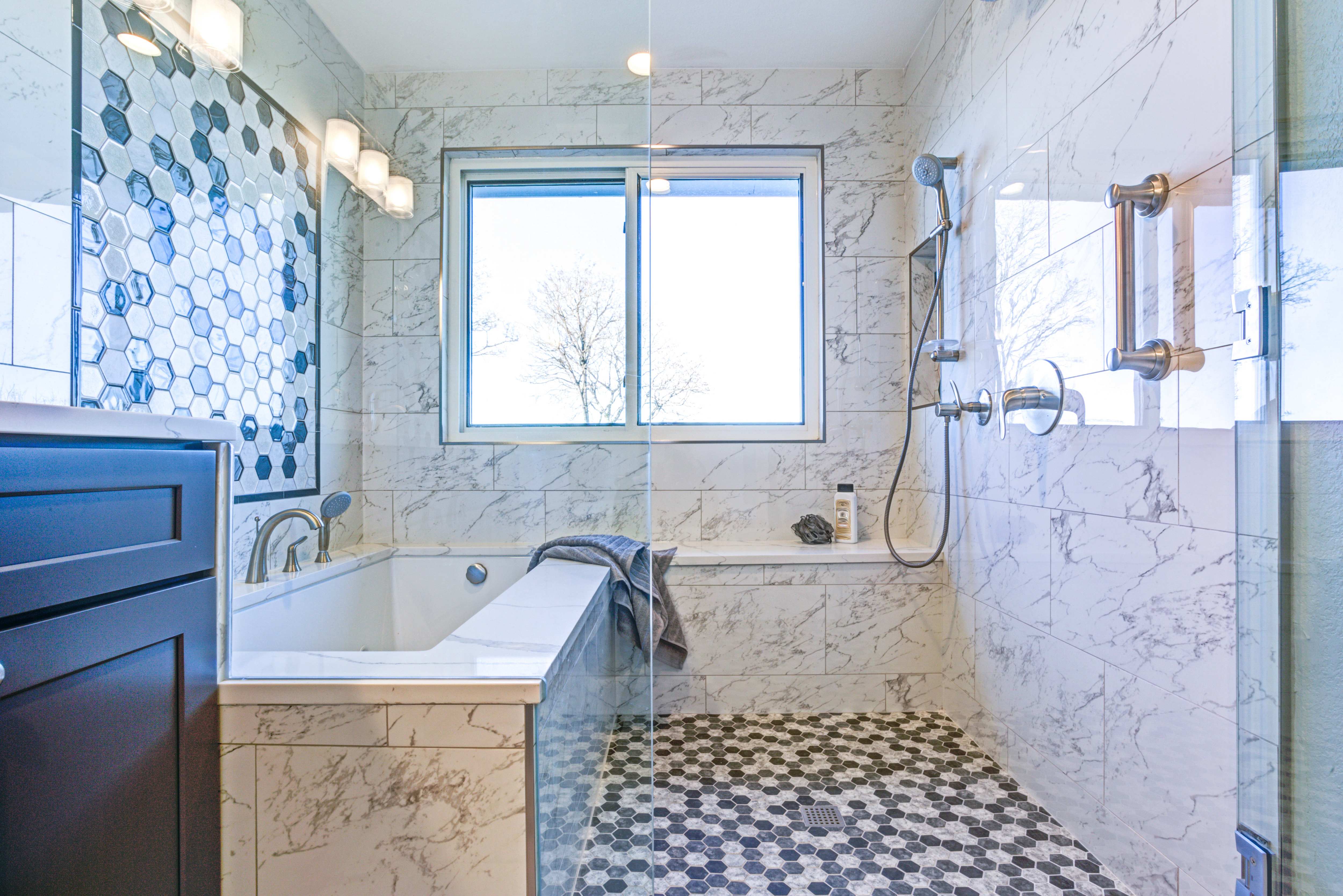 A spa room with a glass door, large bathtub, tile mosaic, and overhead shower