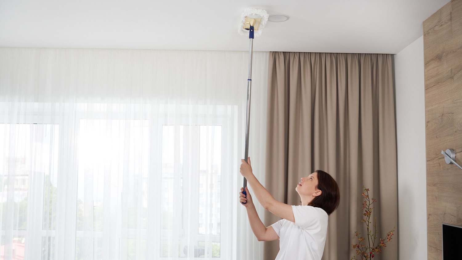 A woman with a mop cleaning a room’s ceiling