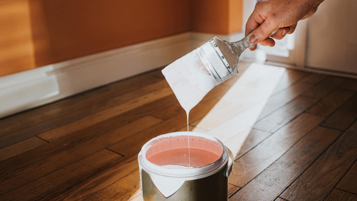 Hand dipping a paint brush into a large tin of paint