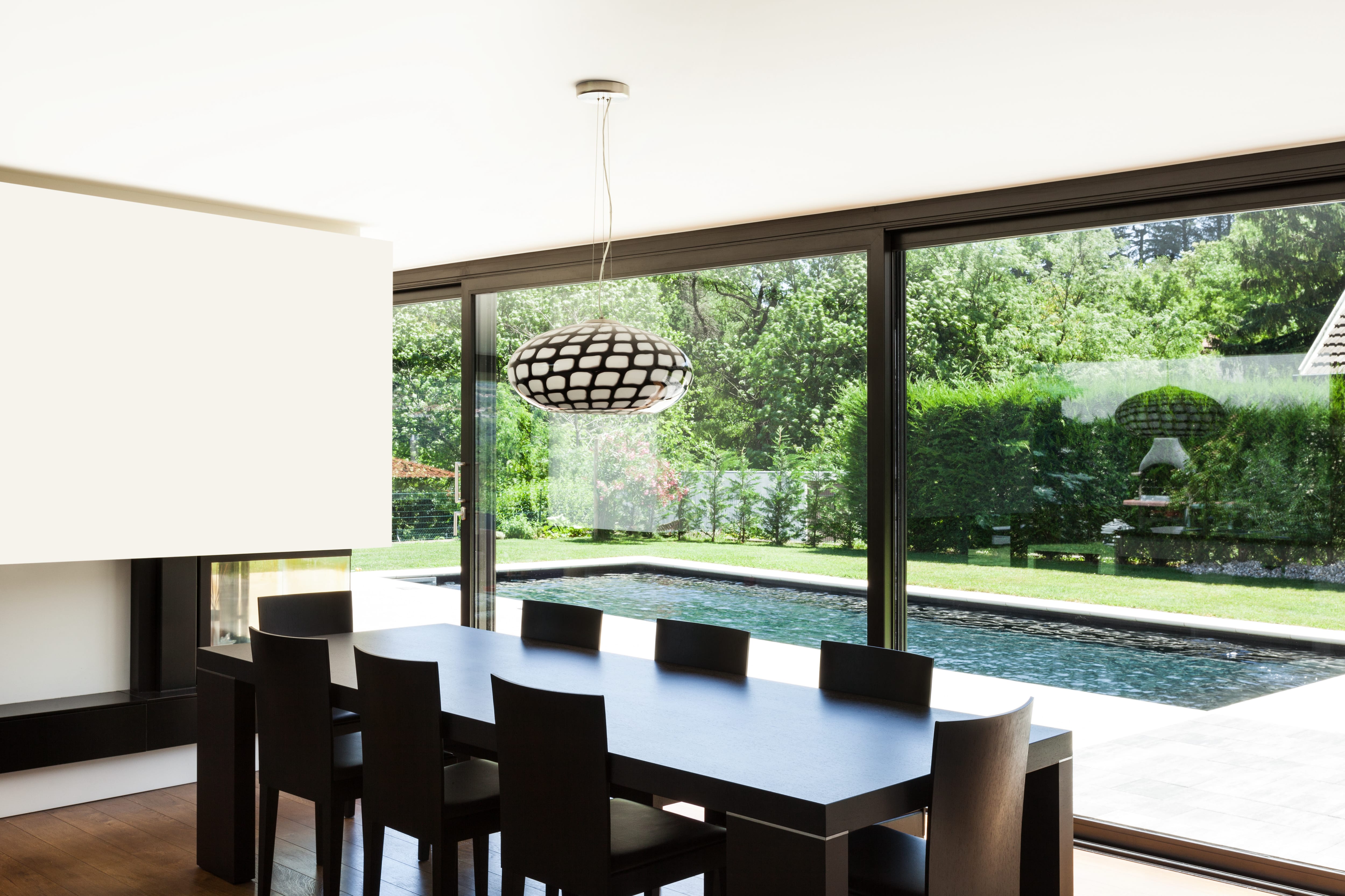 Modern minimalist dining room with black table and chairs overlooking a patio with a pool
