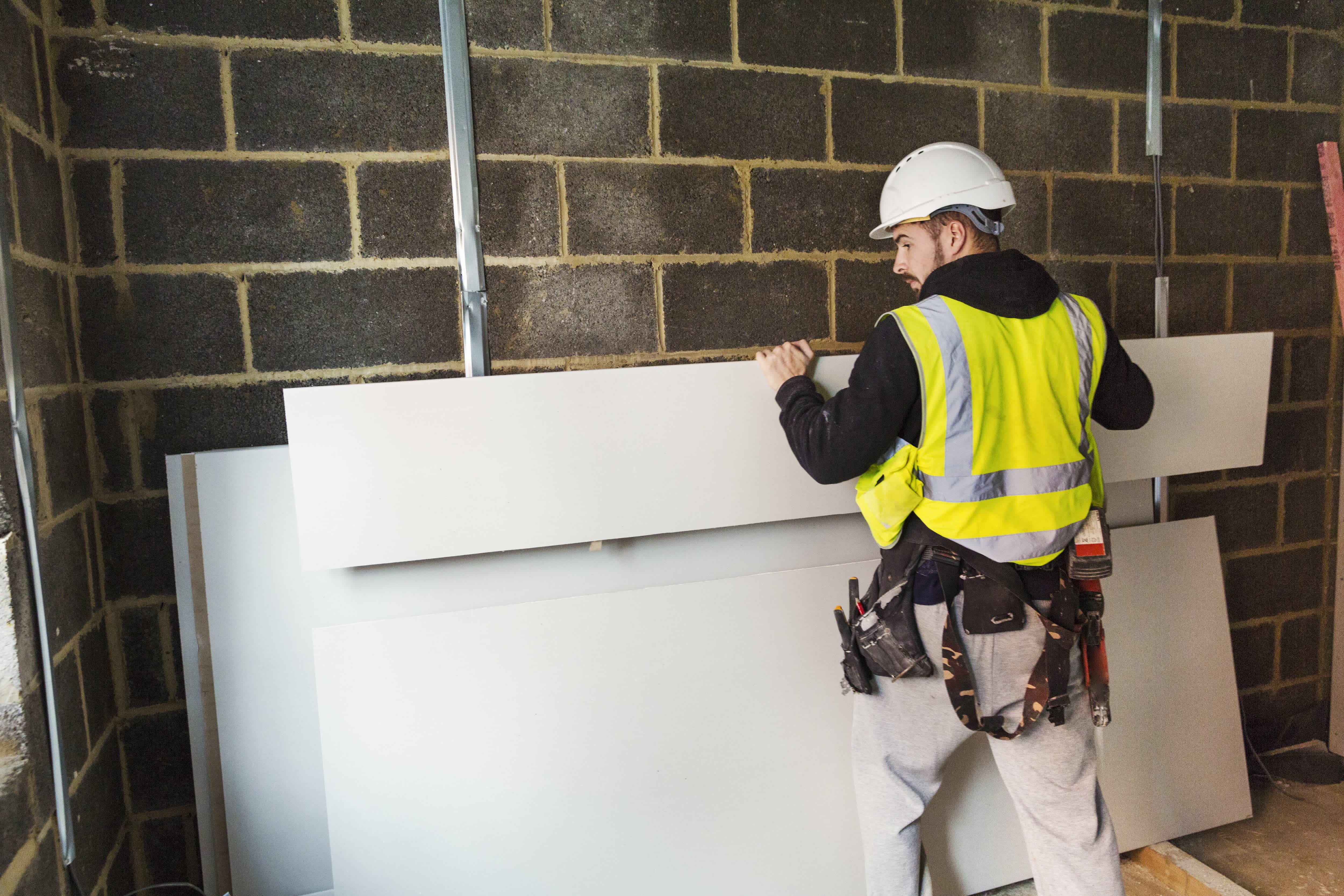 Worker picking up sheet of drywall