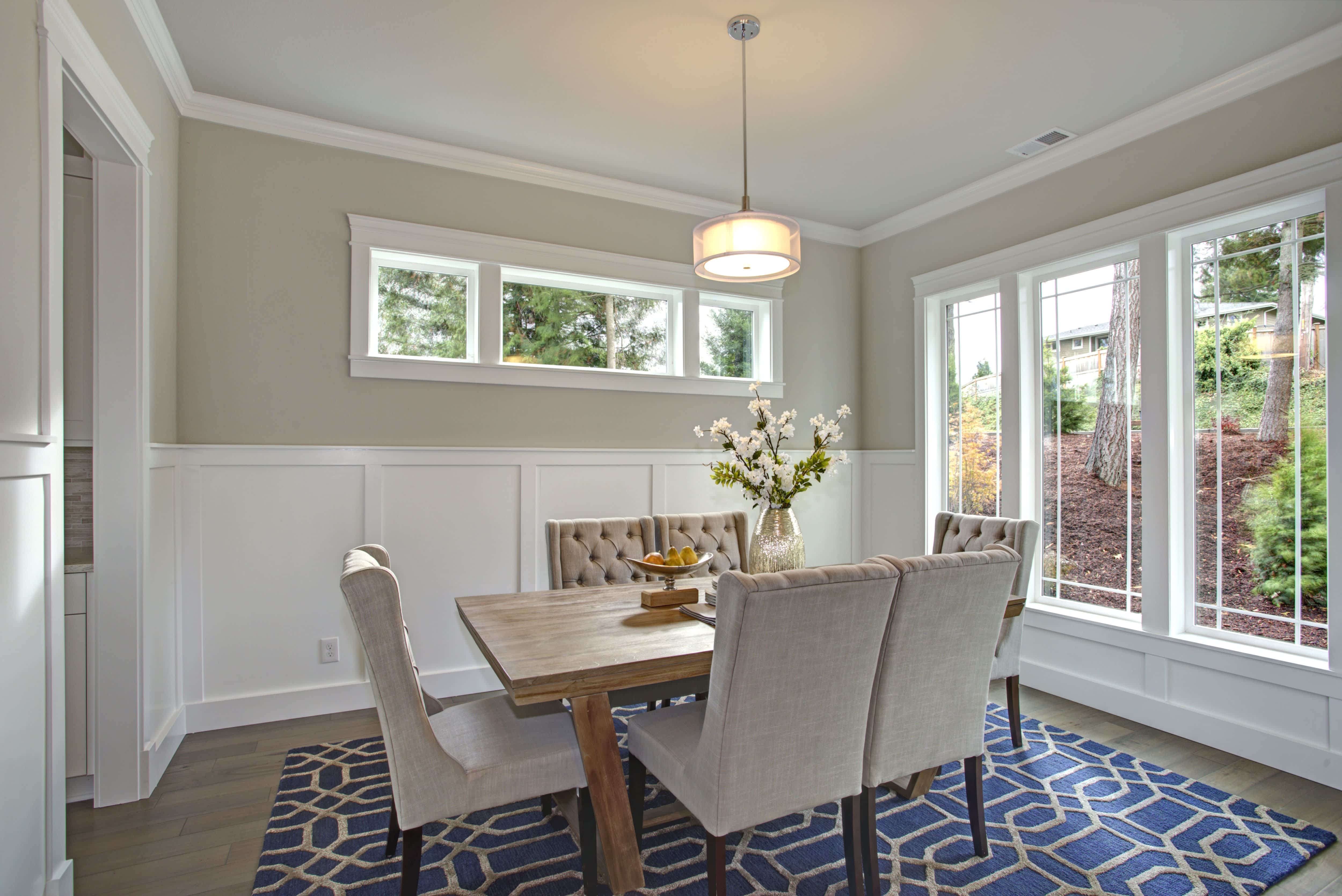 Transitional dining room with board and batten walls, high-backed tufted gray chairs, wood table, and blue geometric rug