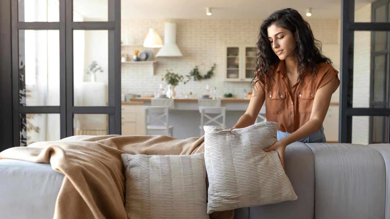 A young woman arranging pillows and a plaid on a sofa