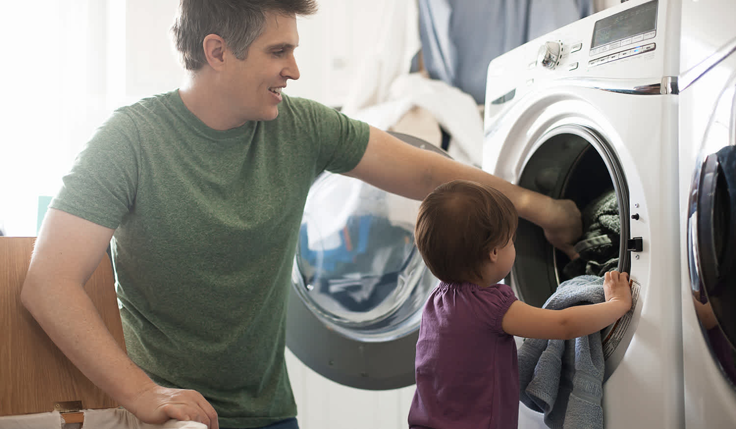 Toddler helps dad put laundry into dryer