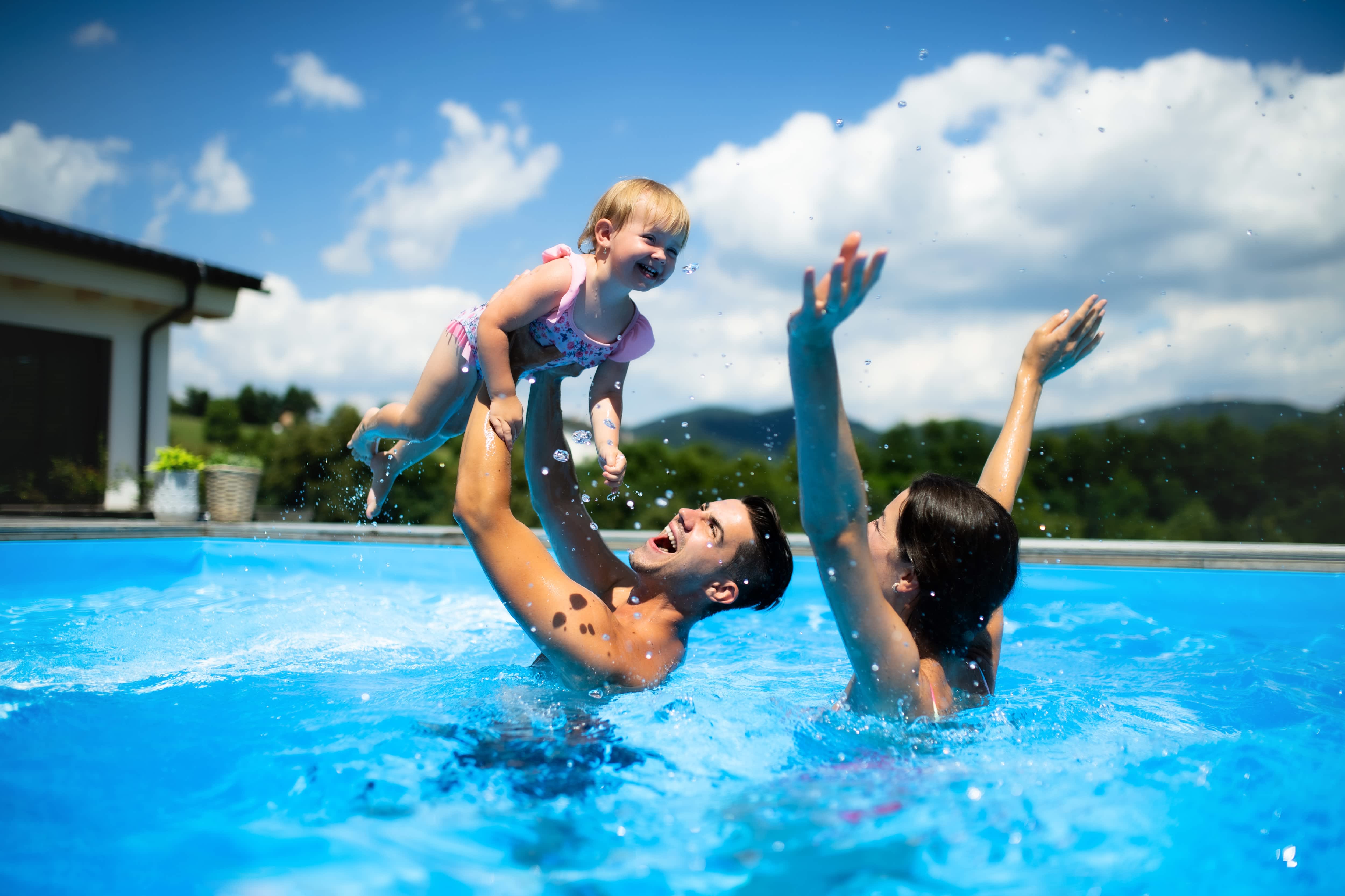 A couple and their baby play in an in-ground pool