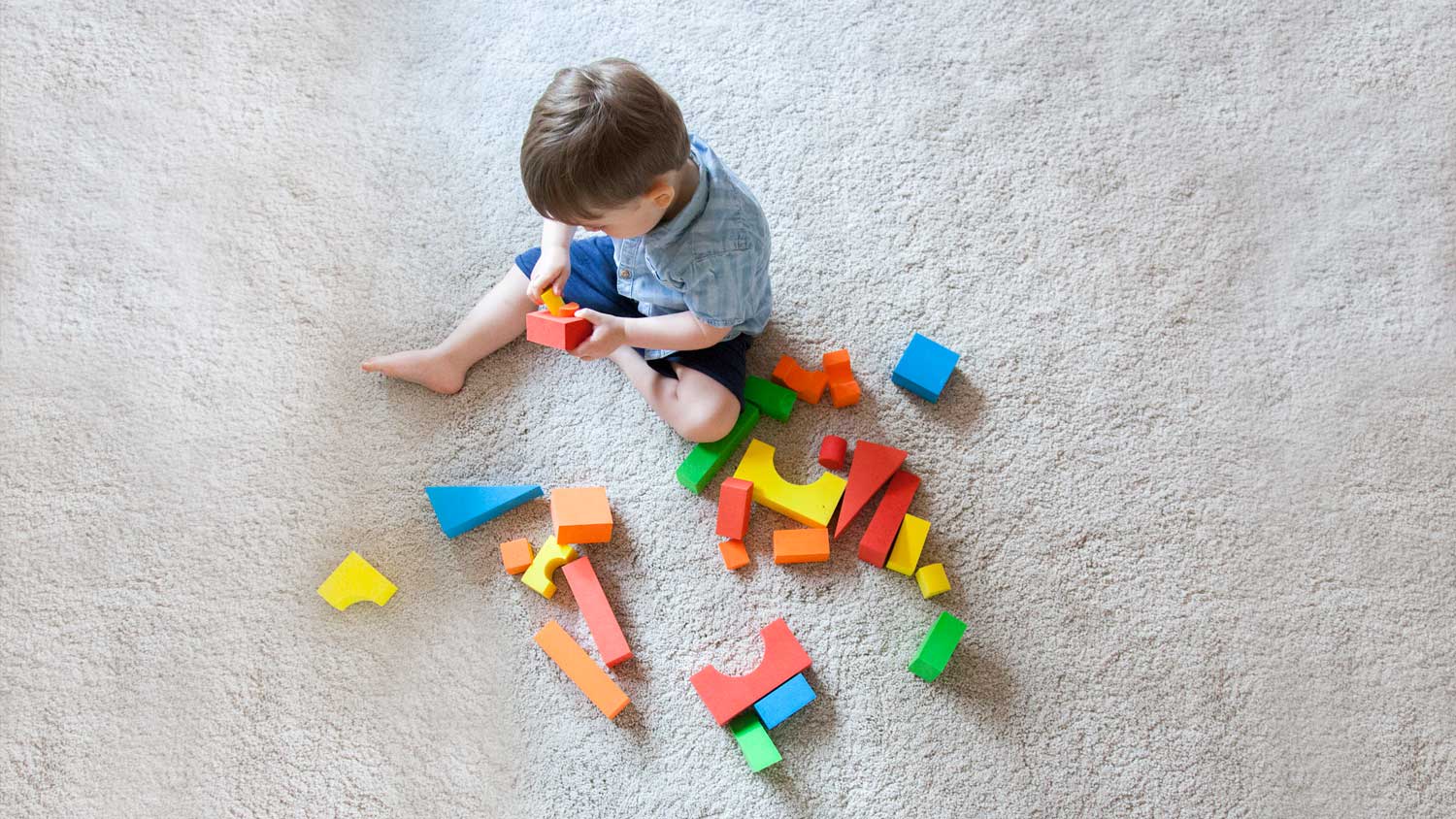 A boy playing with his toys while sitting on the carpet