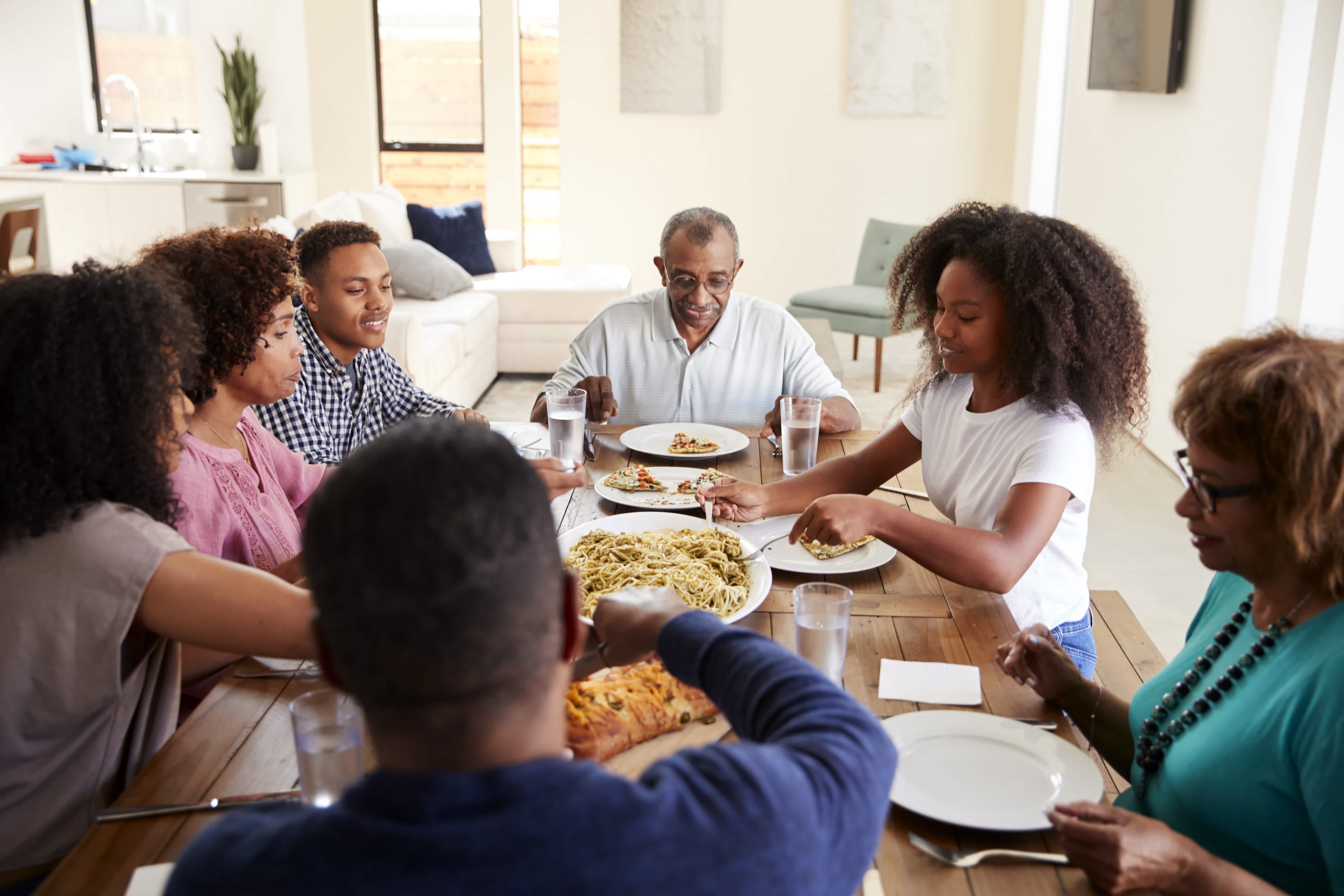 Three generation Black family eating dinner together at wood dining room table