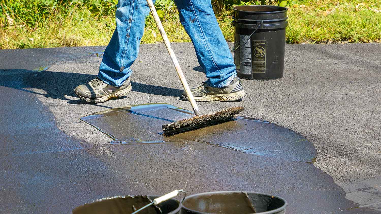 Worker using a brush to apply sealant on the driveway