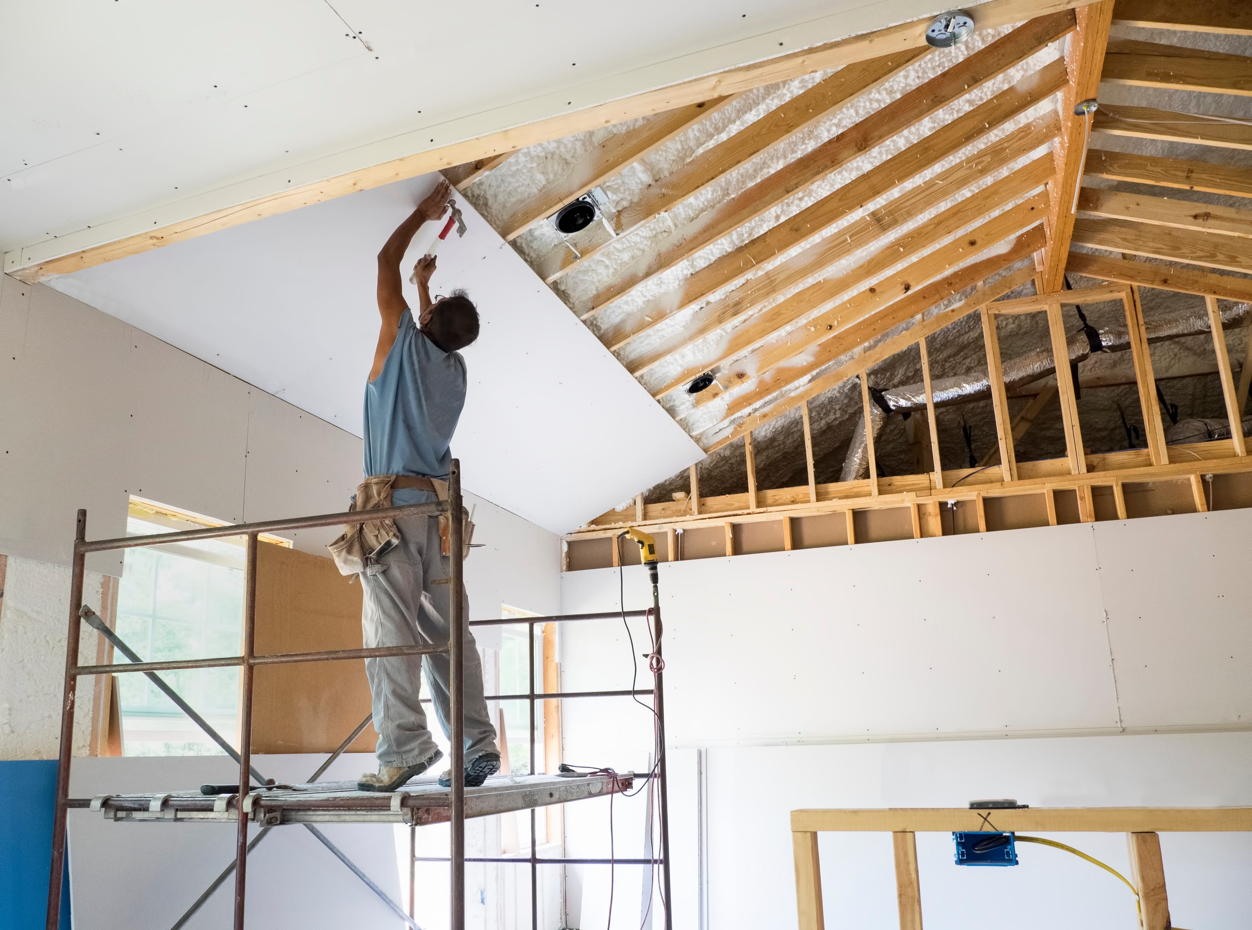 Worker installing Sheetrock over ceiling joists
