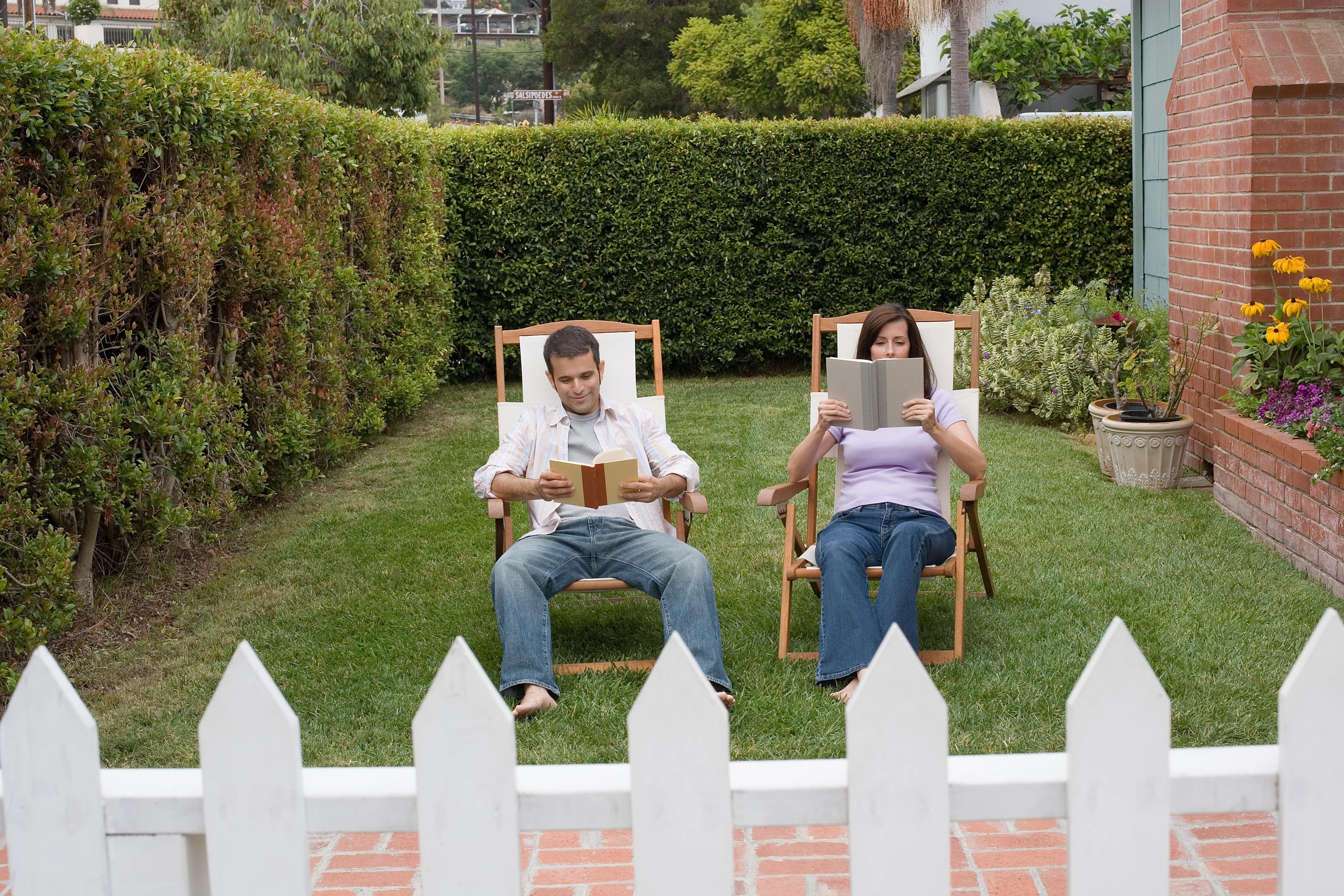 A man and woman sitting in lounge chairs in a backyard surrounded by tall privet hedges