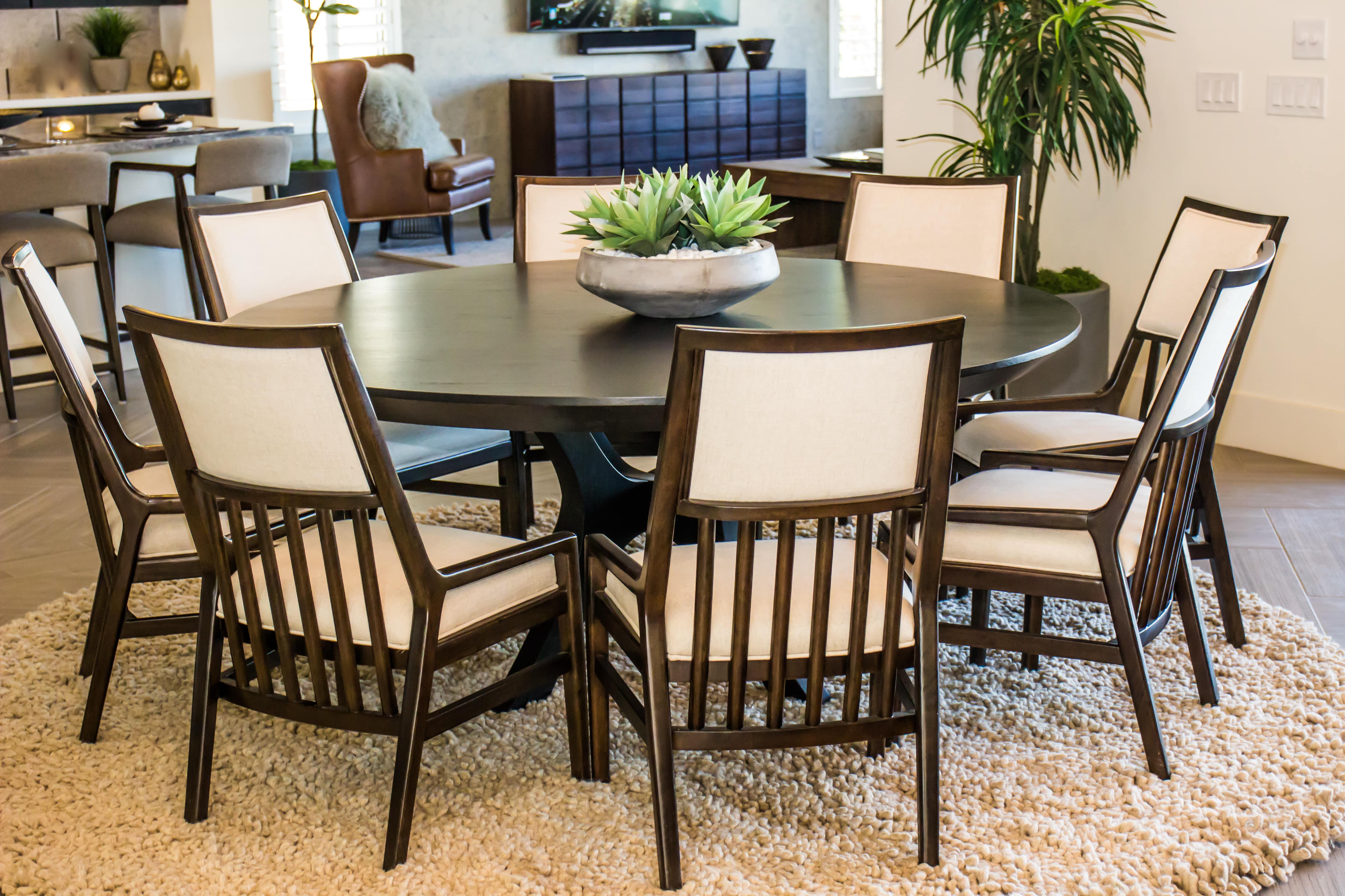 Brown wood round dining table with eight cream-colored chairs