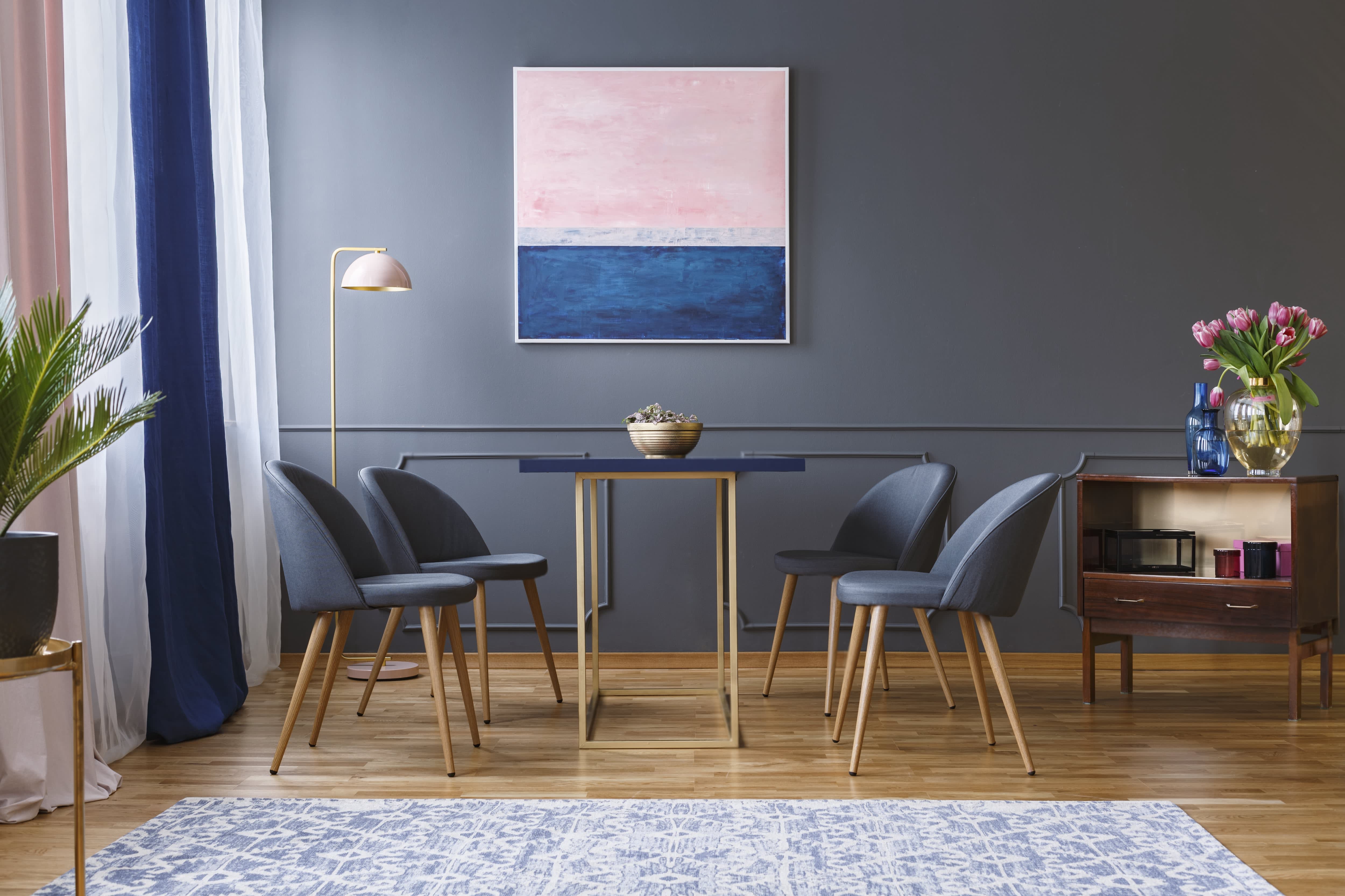 Modern dining room with dark gray walls and chairs, navy table, navy, and pink curtains, and abstract navy and pink painting