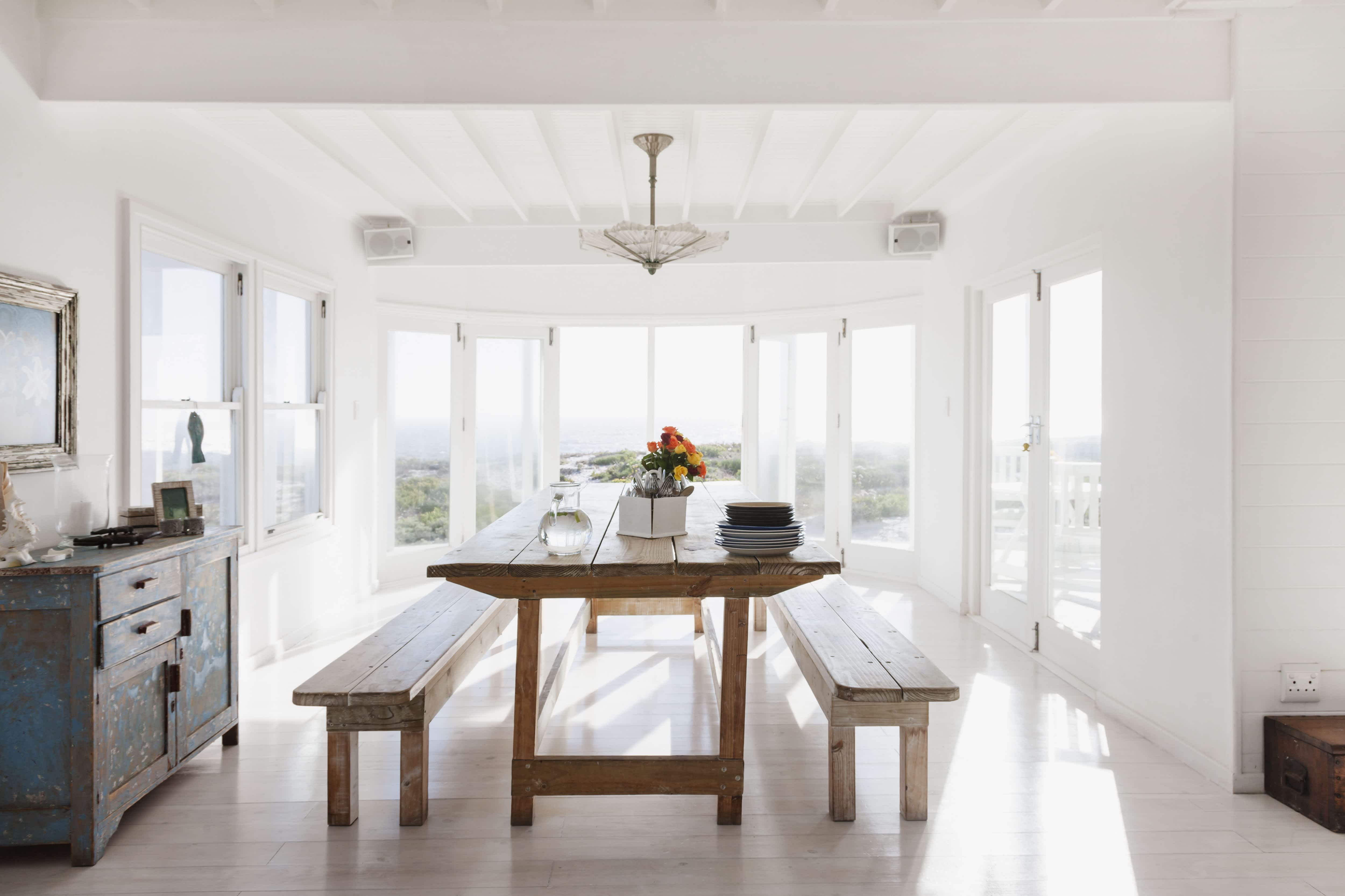 Sunny all-white dining room with rustic wood dining table with two benches