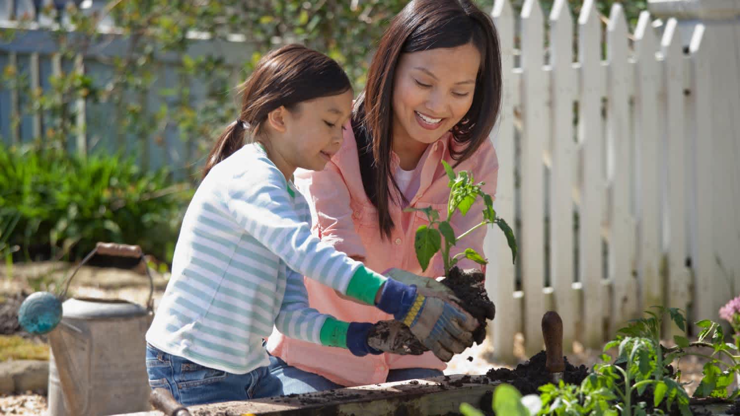 A mother and her daughter planting and watering their garden