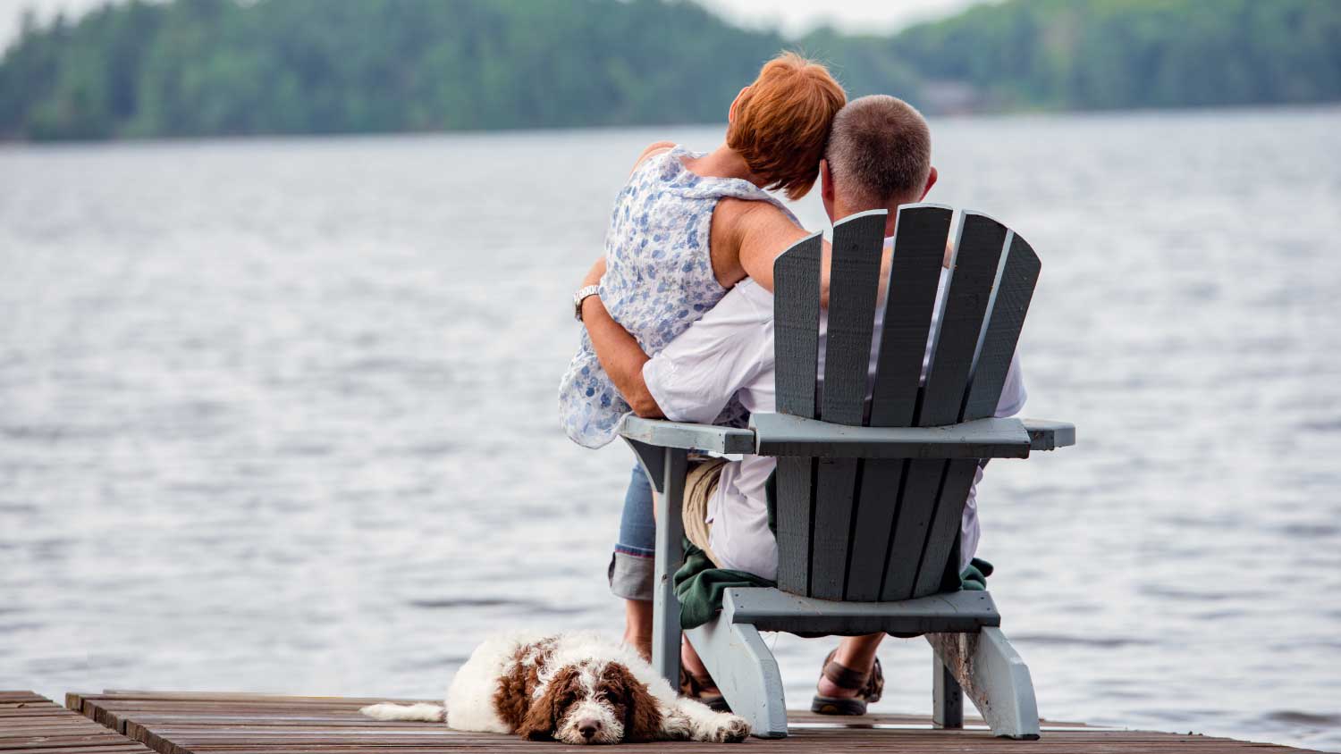 couple sitting in adirondack style chair on lake
