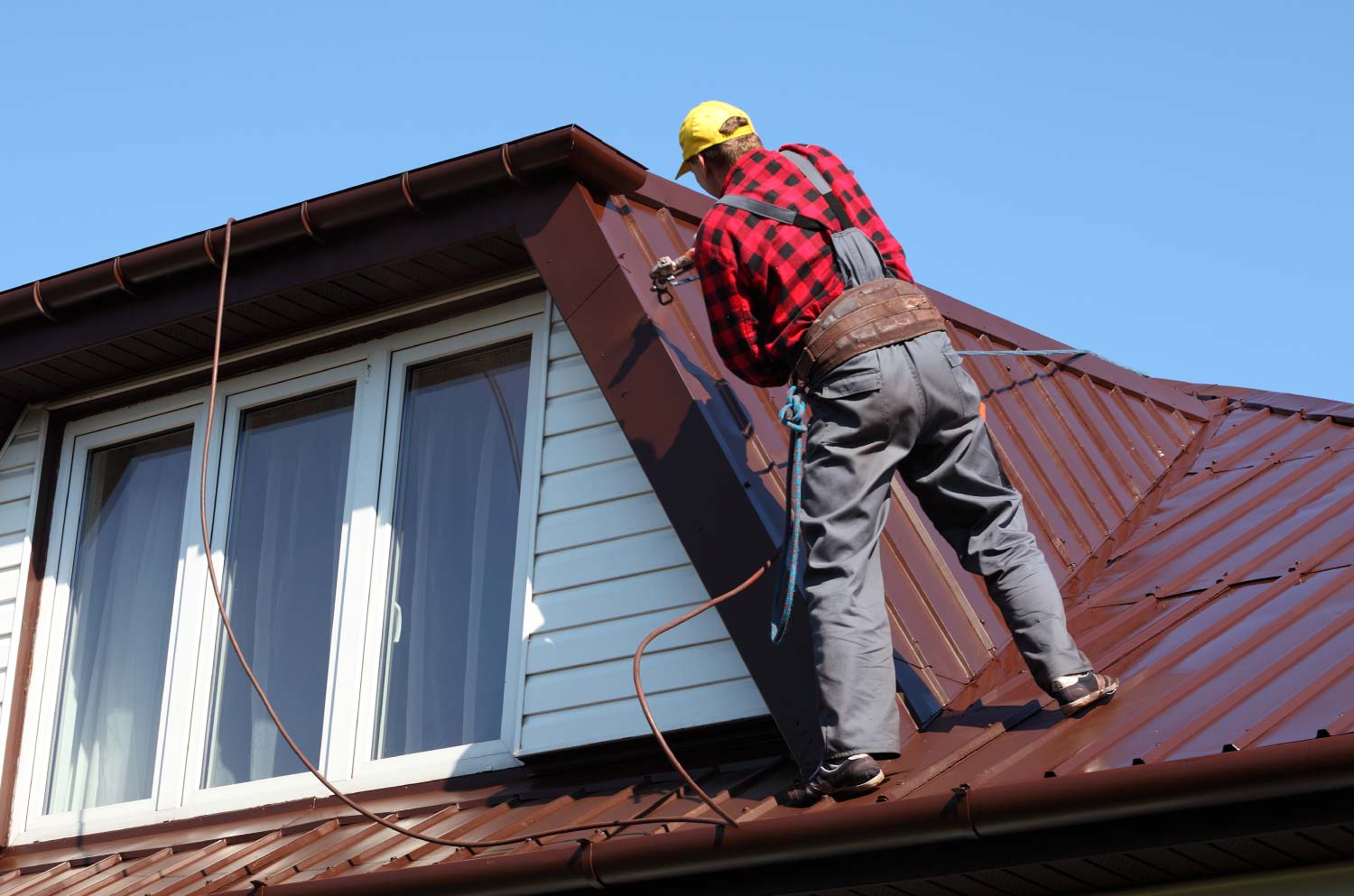 Worker spraying paint on metal sheet roof