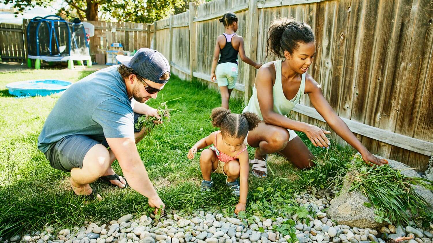 A family pulling weeds from gravel in the garden