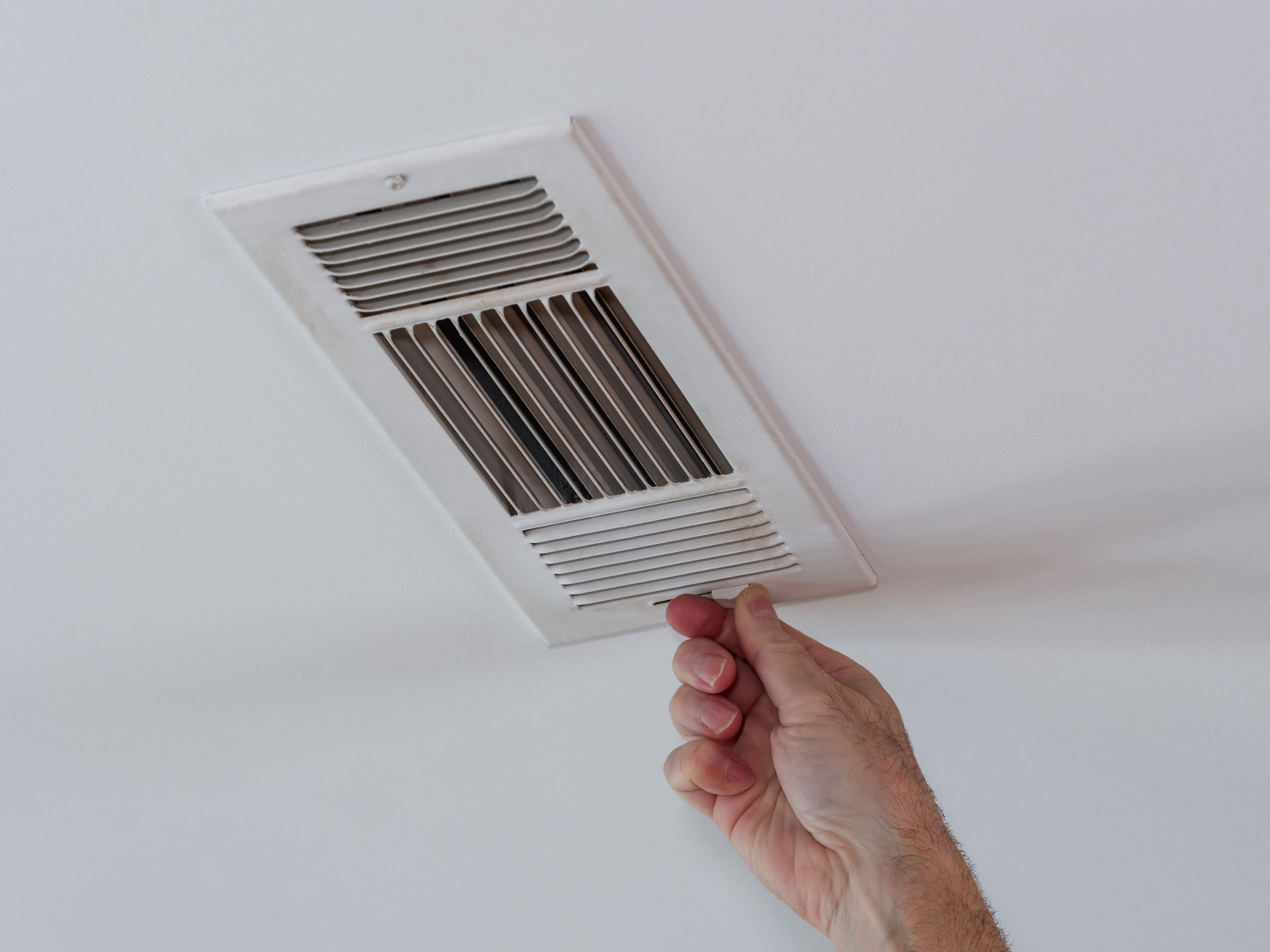 A person adjusting a ceiling vent for an HVAC system