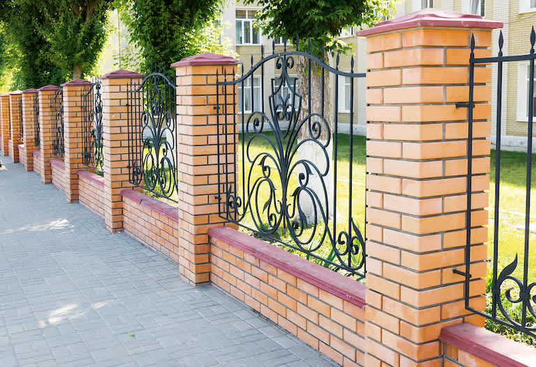 a tan brick fence with alternating metal grille design and stone sidewalk