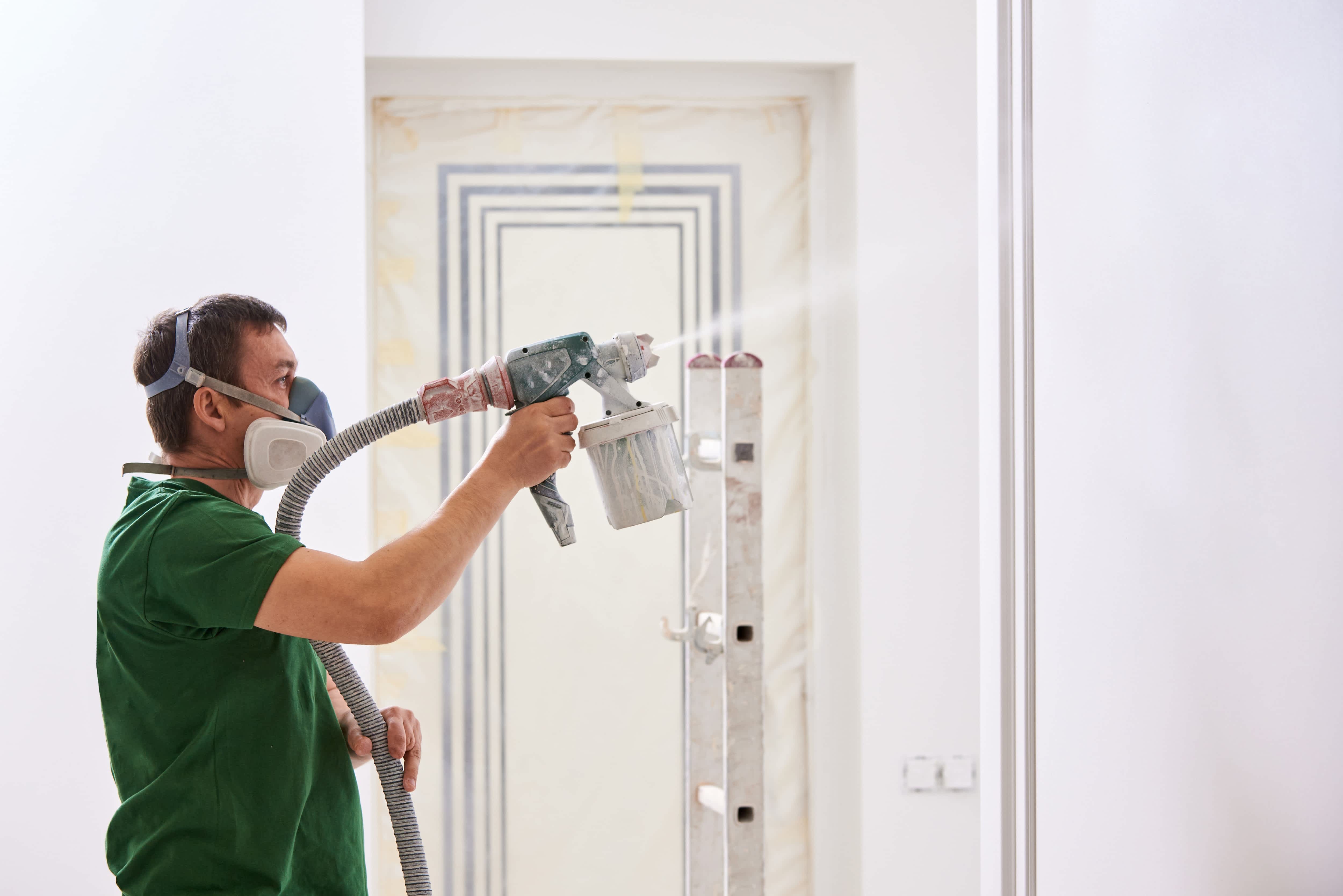 Man using paint sprayer to paint a wall white