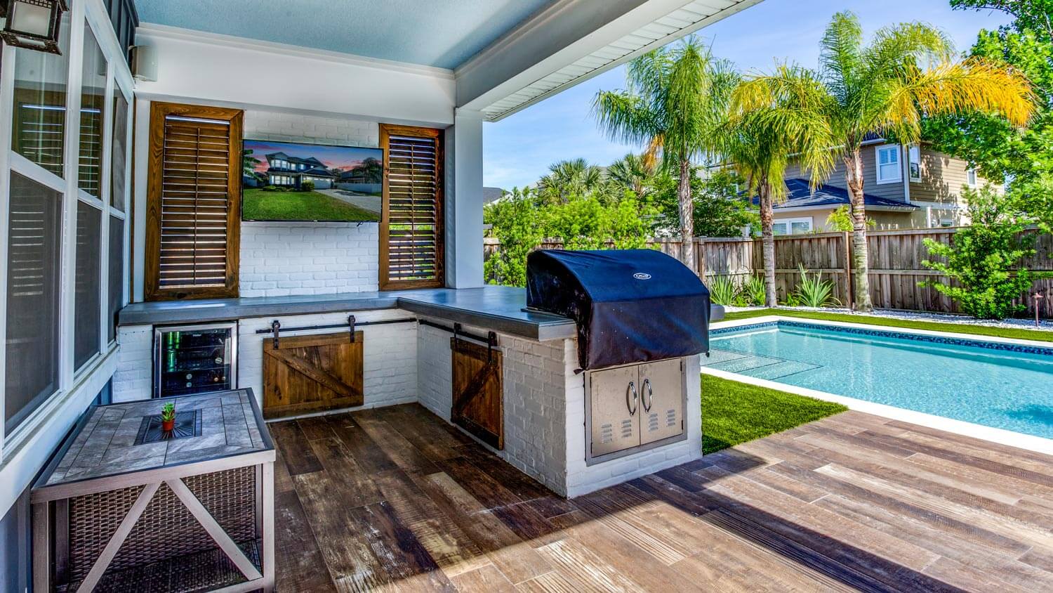 A backyard pool with an outdoor kitchen and a TV