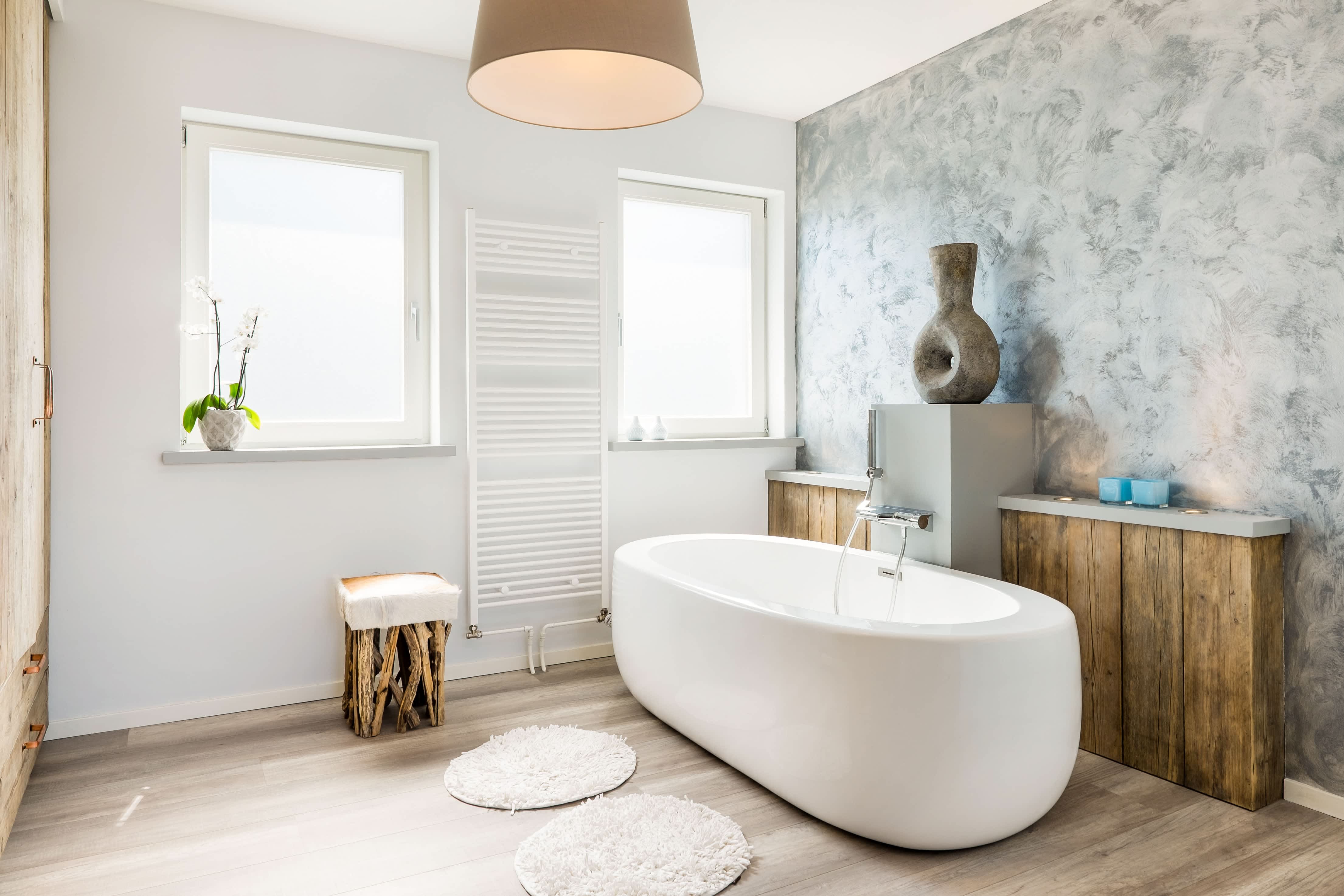 Modern bathroom with light wood floors, a white bathtub, and a watercolor wallpaper accent wall