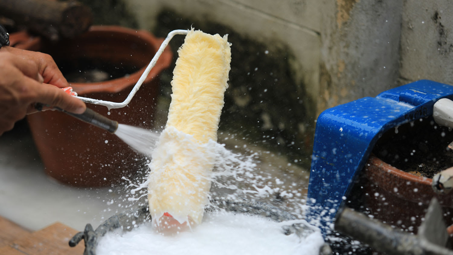 A man cleaning a paint roller with a water hose