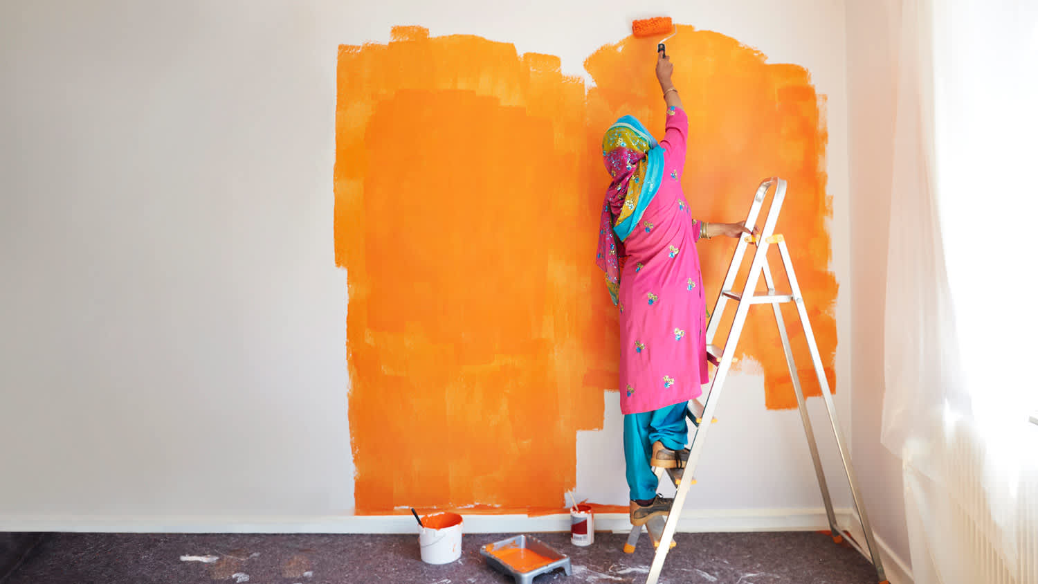 A woman on a ladder painting a room with a paint roller