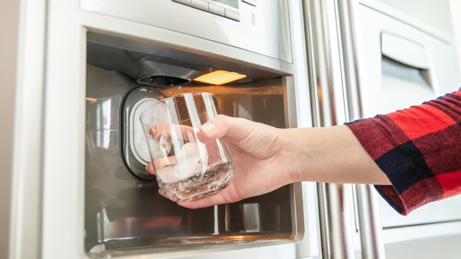 A woman holding a glass and using refrigerator to make fresh ice cubes