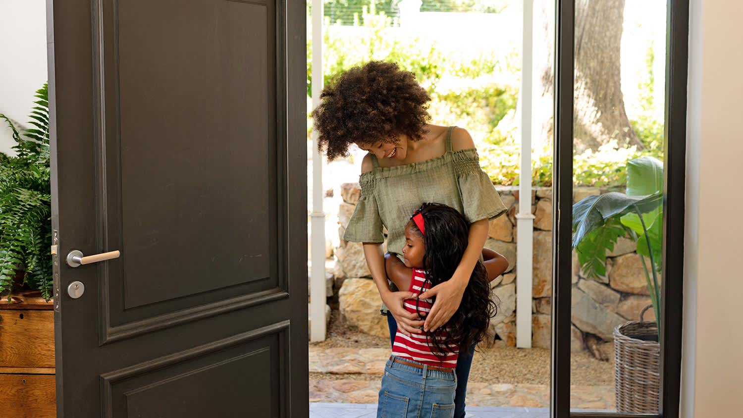 Mom hugs little girl at front door