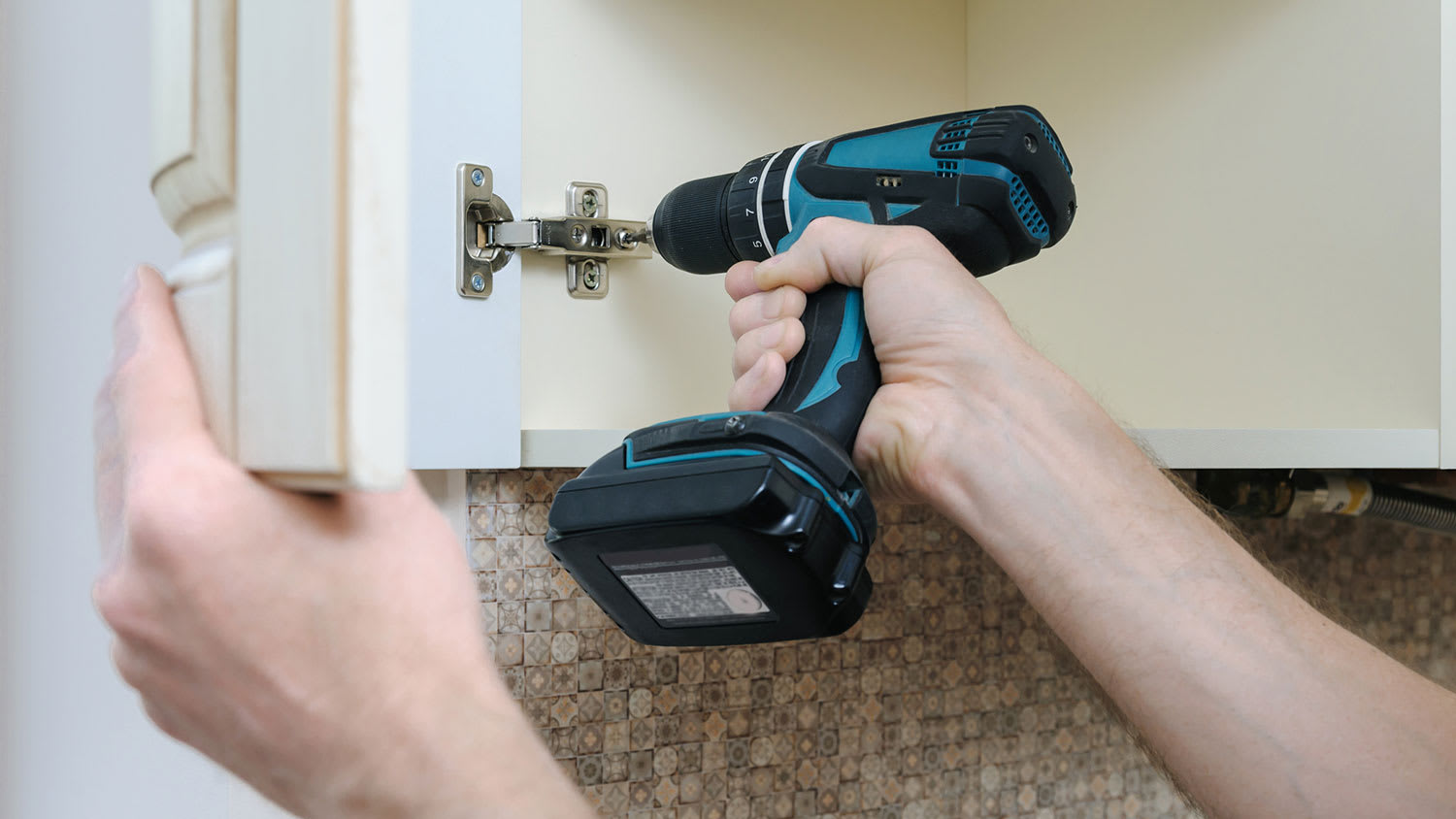 Carpenter using electric screwdriver to adjust a cabinet hinge