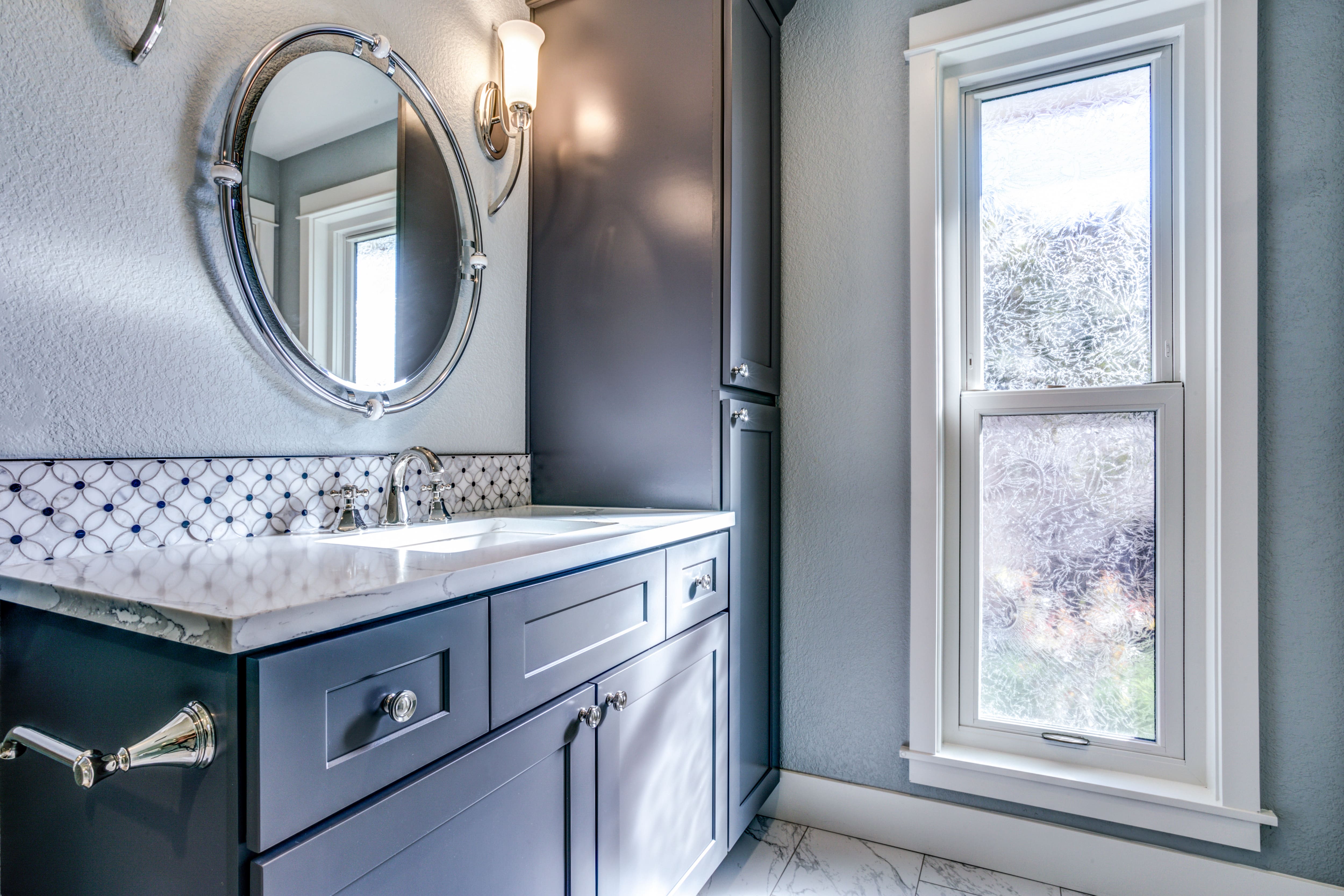 Modern bathroom with blue walls, navy vanity, silver mirror, and mosaic backsplash