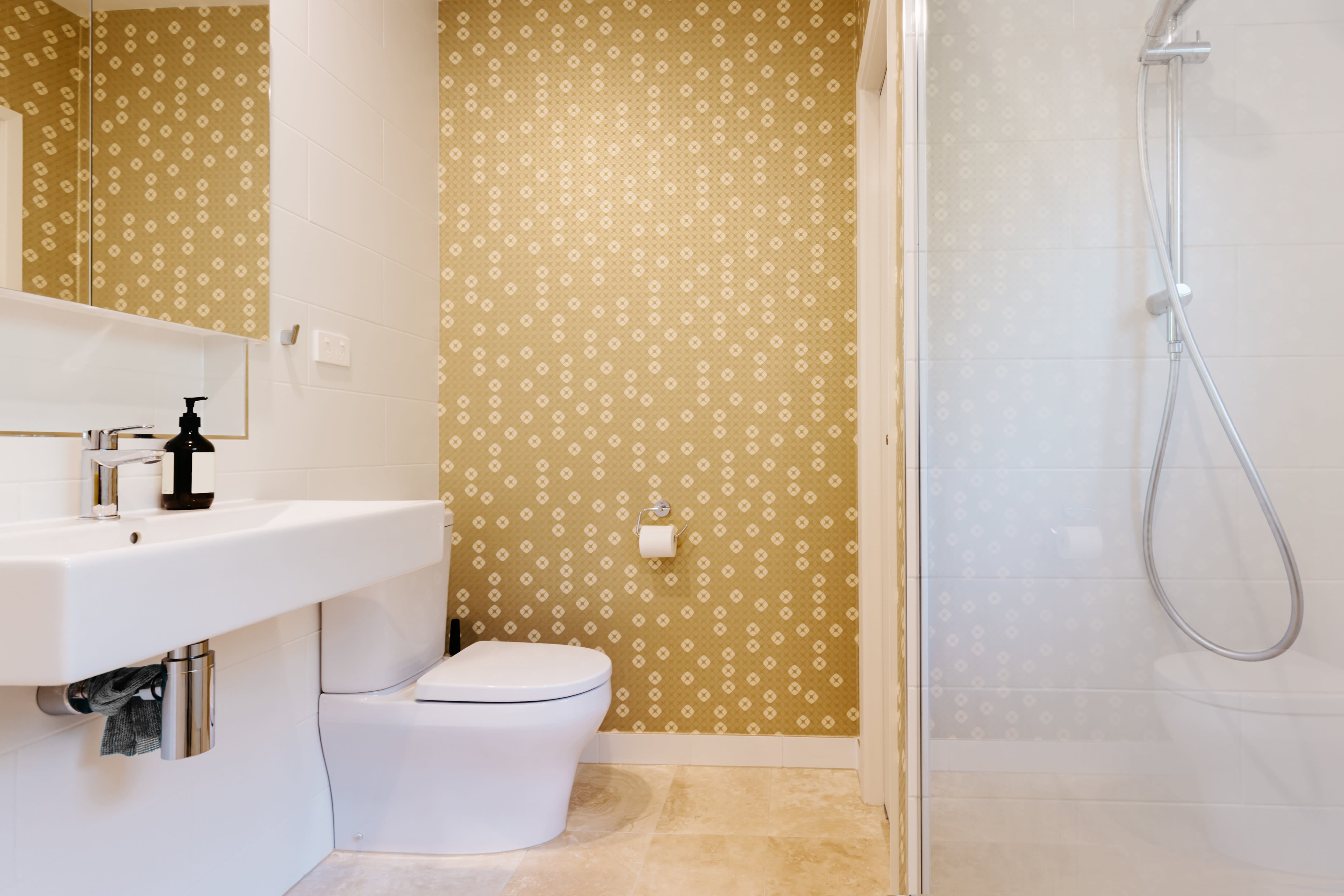 Small bathroom with gold wallpaper, shower, and a white sink