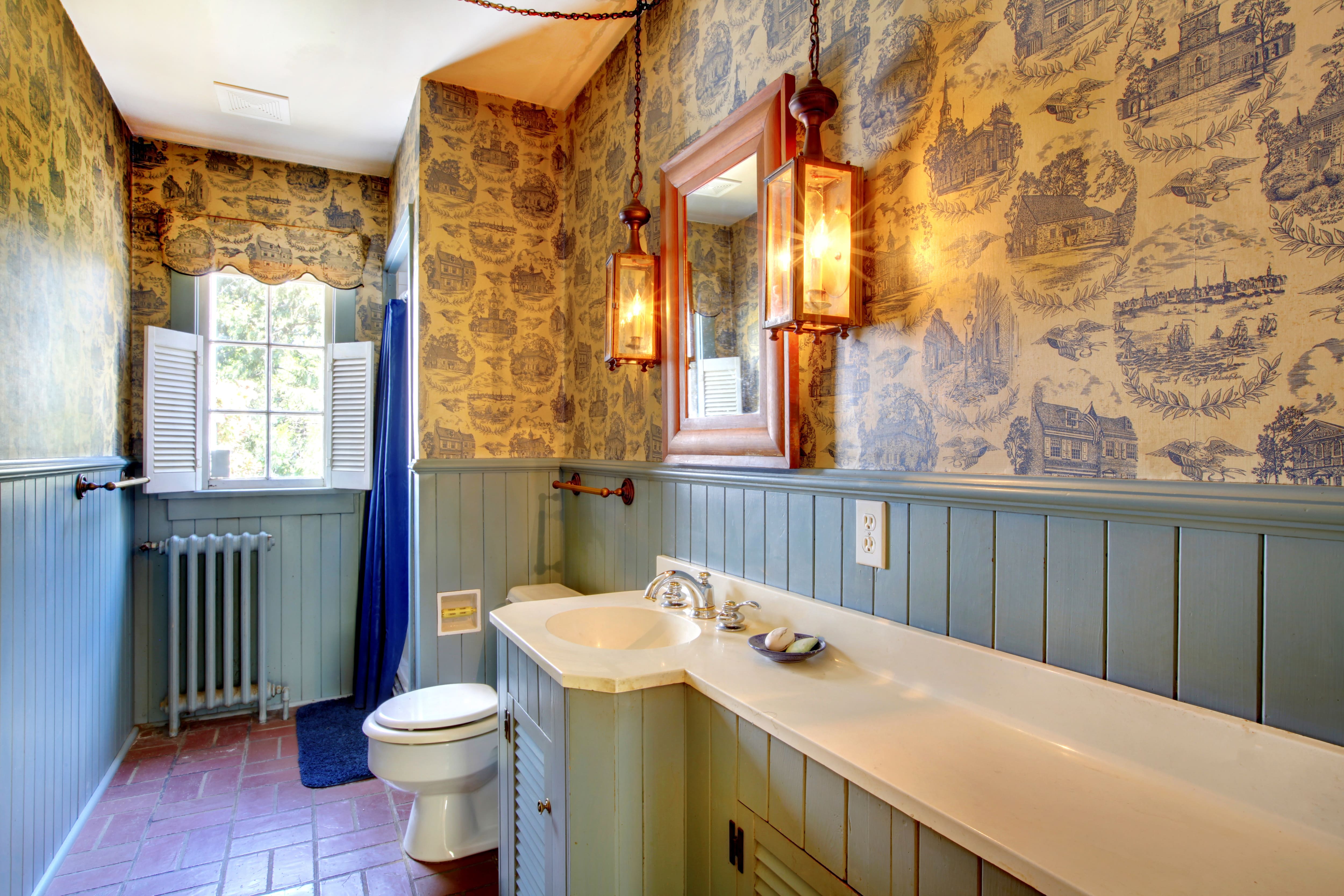 Vintage bathroom with toile wallpaper, green cabinets, and brick floors