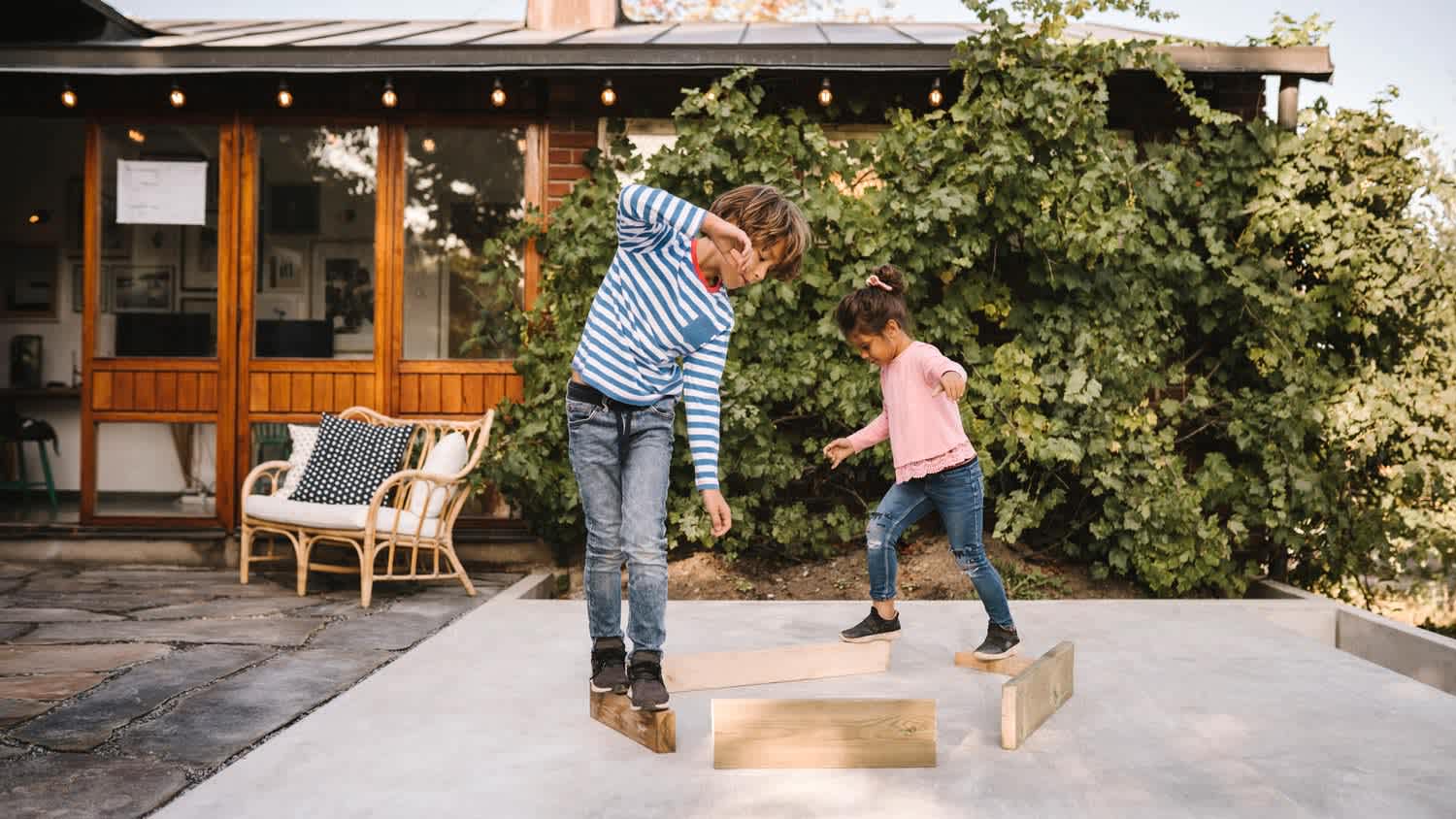 Siblings balancing on wooden planks placed on a concrete slab