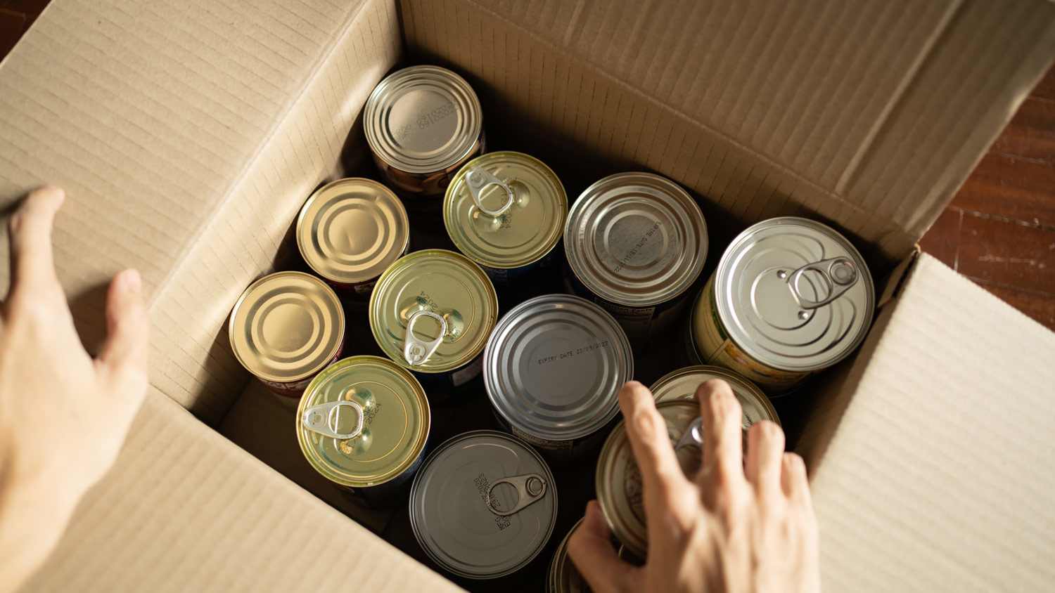 A hand placing canned food in a cardboard box