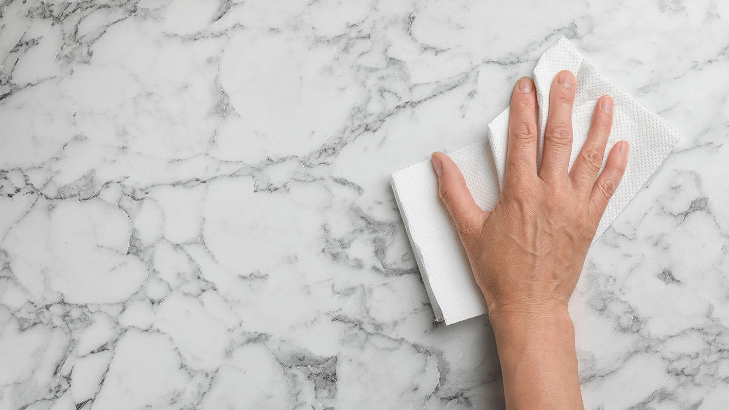 A hand wipes a marble surface with a paper towel