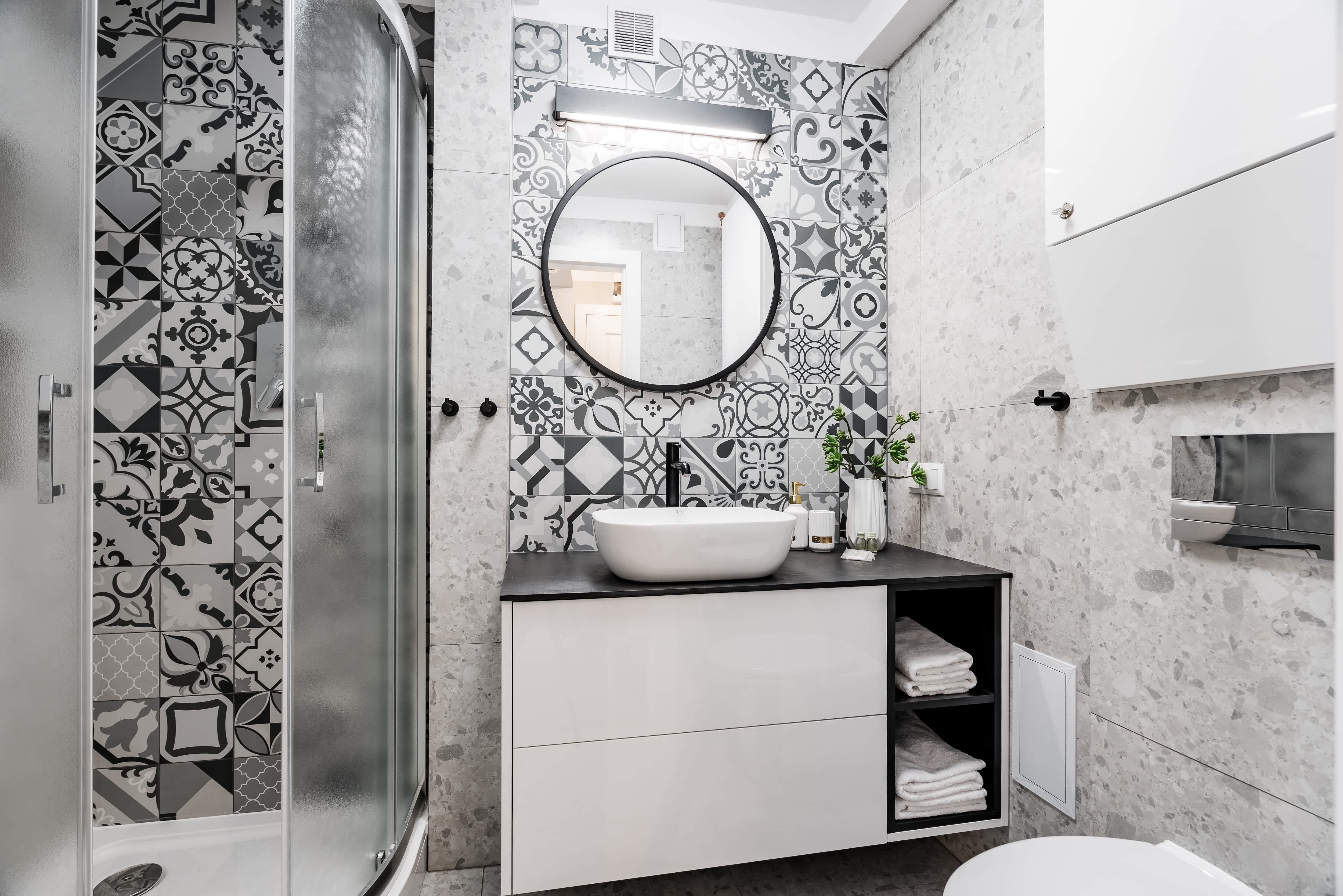 Small bathroom with black-and-white mosaic tiles, a round mirror, and white vanity