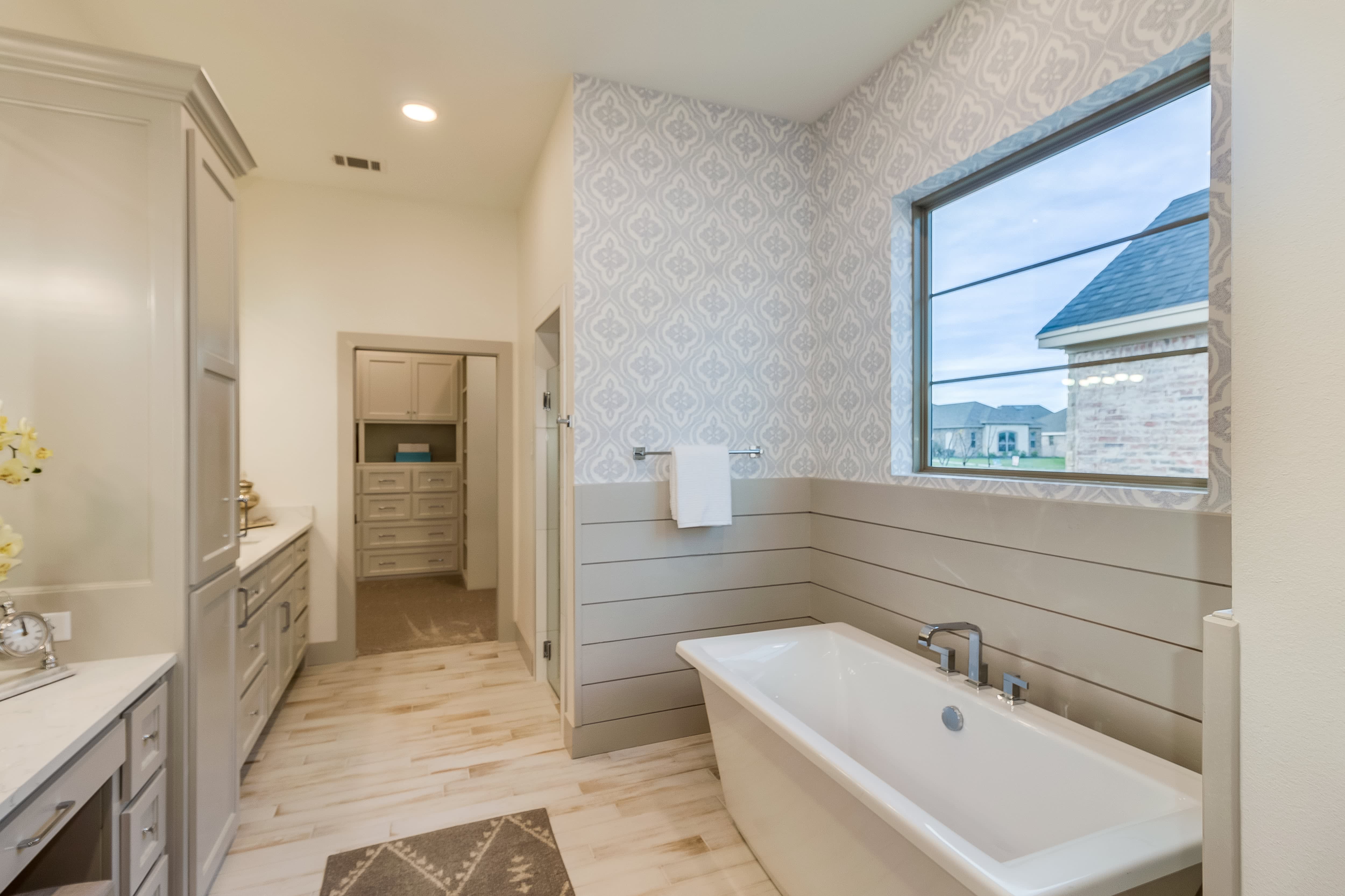 Large bathroom with wooden floors, gray shiplap walls, and patterned wallpaper
