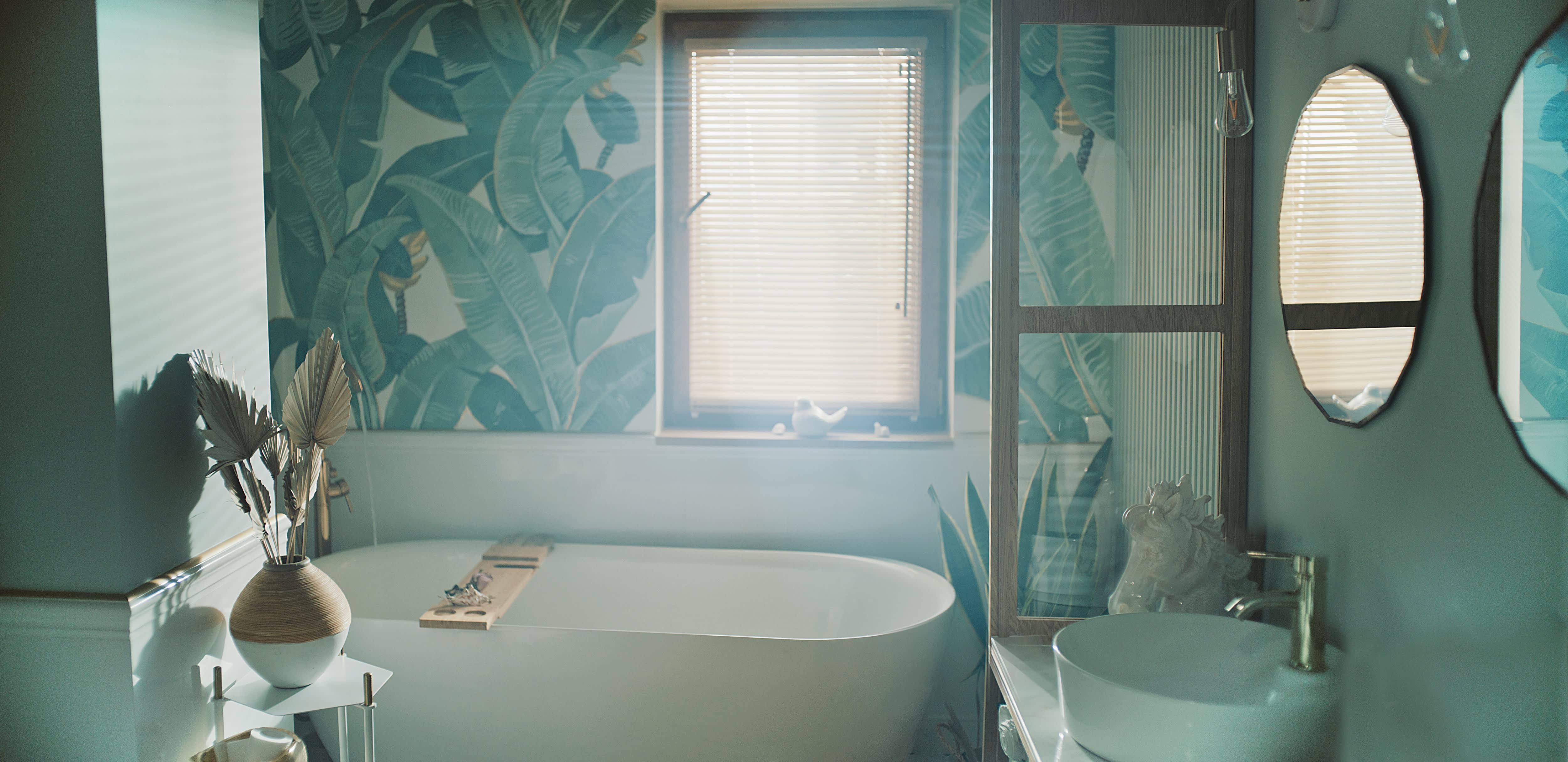 Bathroom with wallpaper featuring palm leaves, a white bathtub, mirrors, and sink