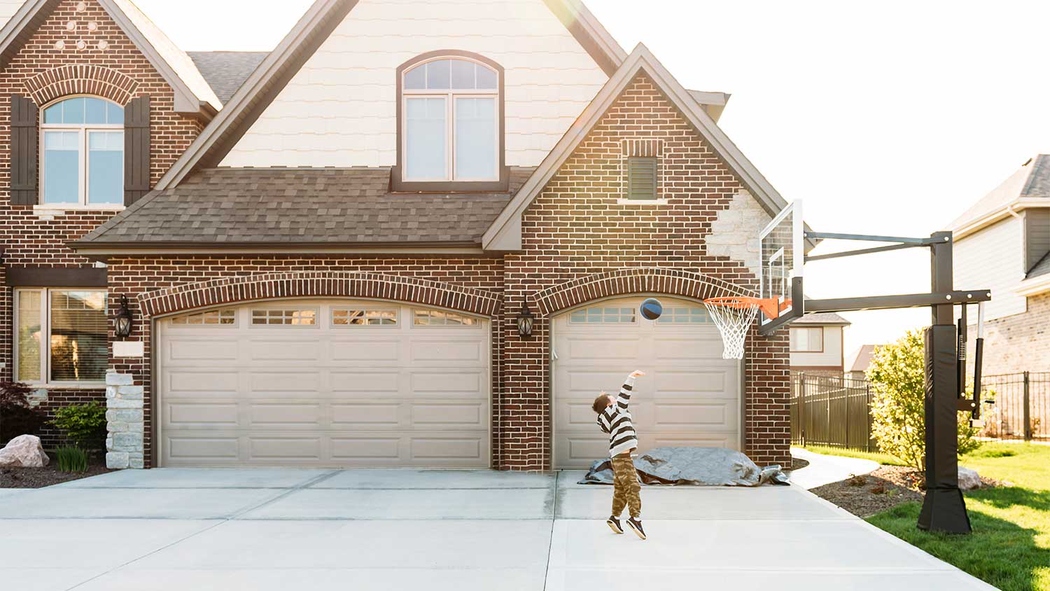 A child plays basketball in front of a garage