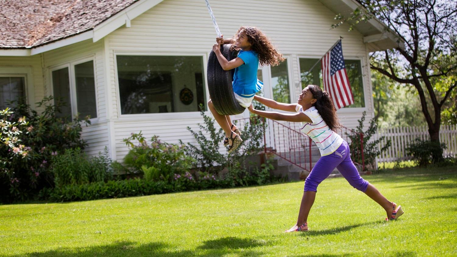 Sisters playing on a tire swing on a house’s yard
