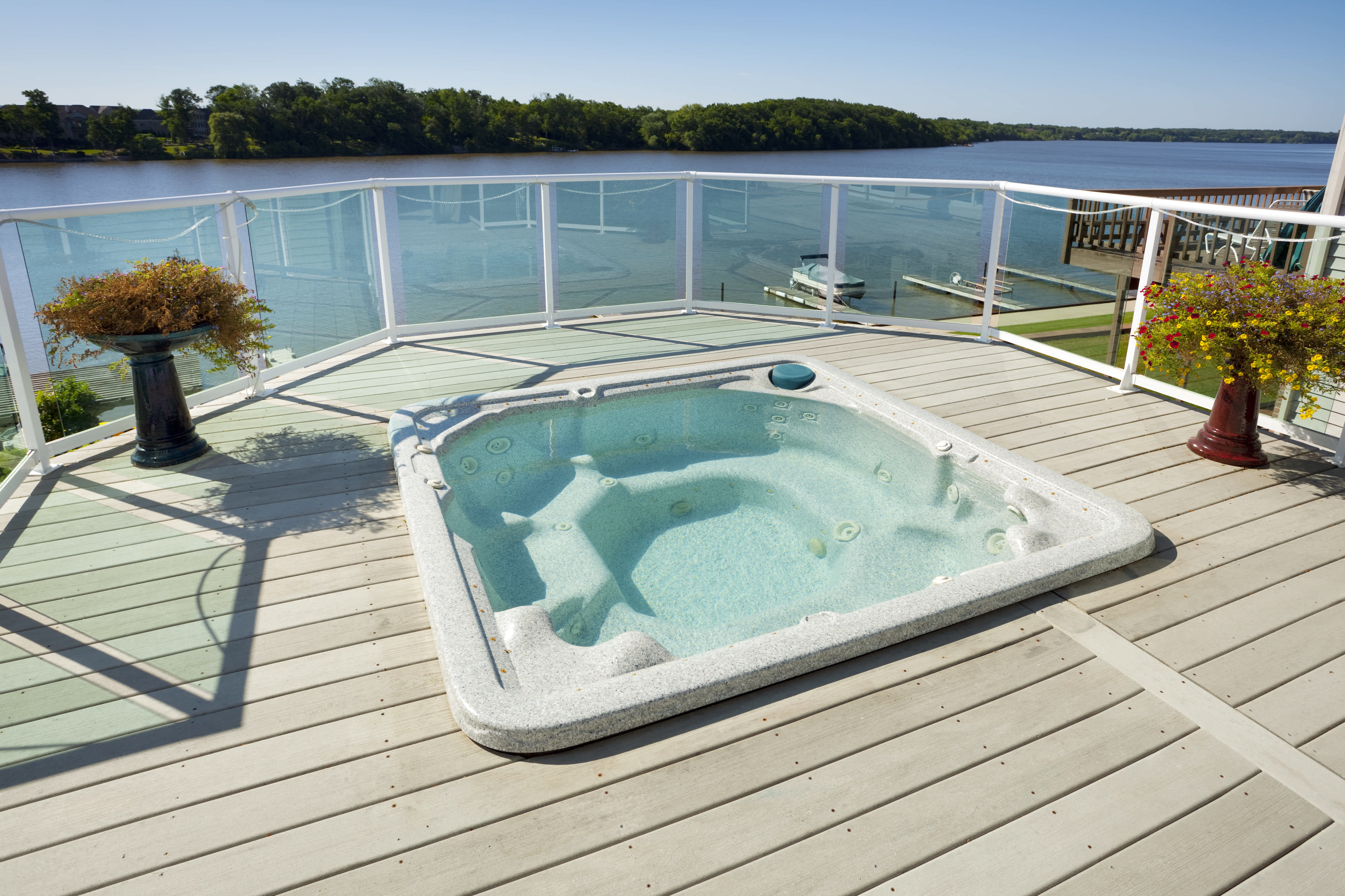 A back deck overlooking the water with a hot tub and glass panel railings