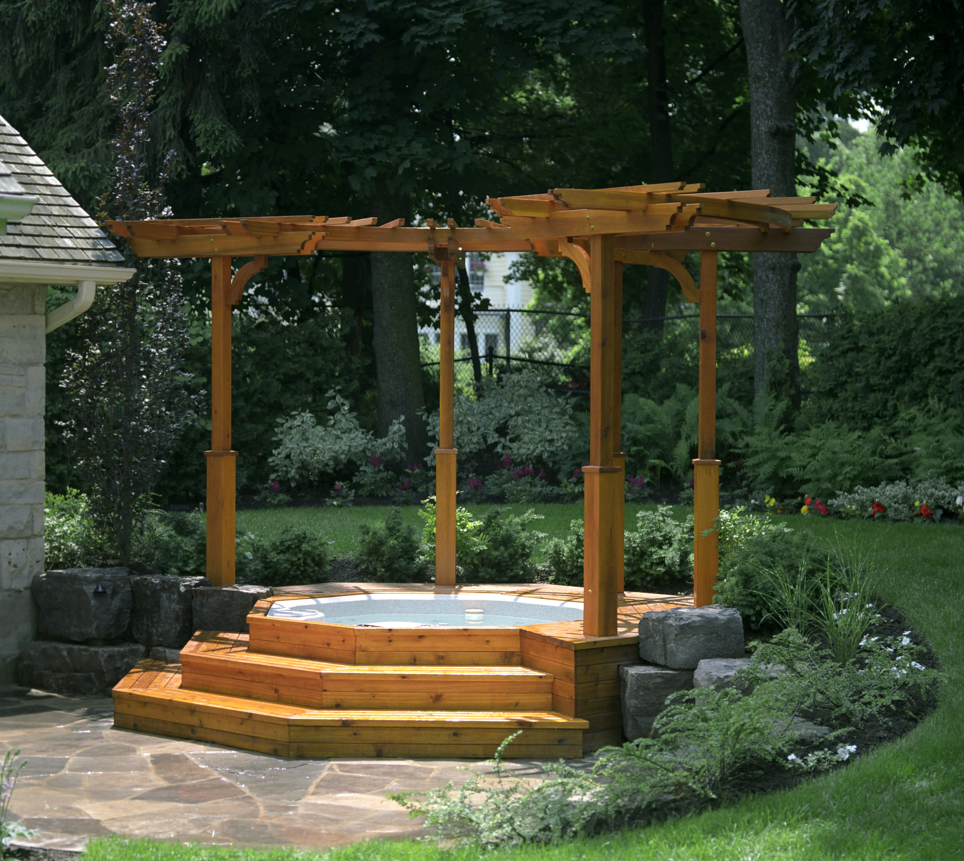 A hot tub off to the side of a patio with a simplistic pergola overtop of it