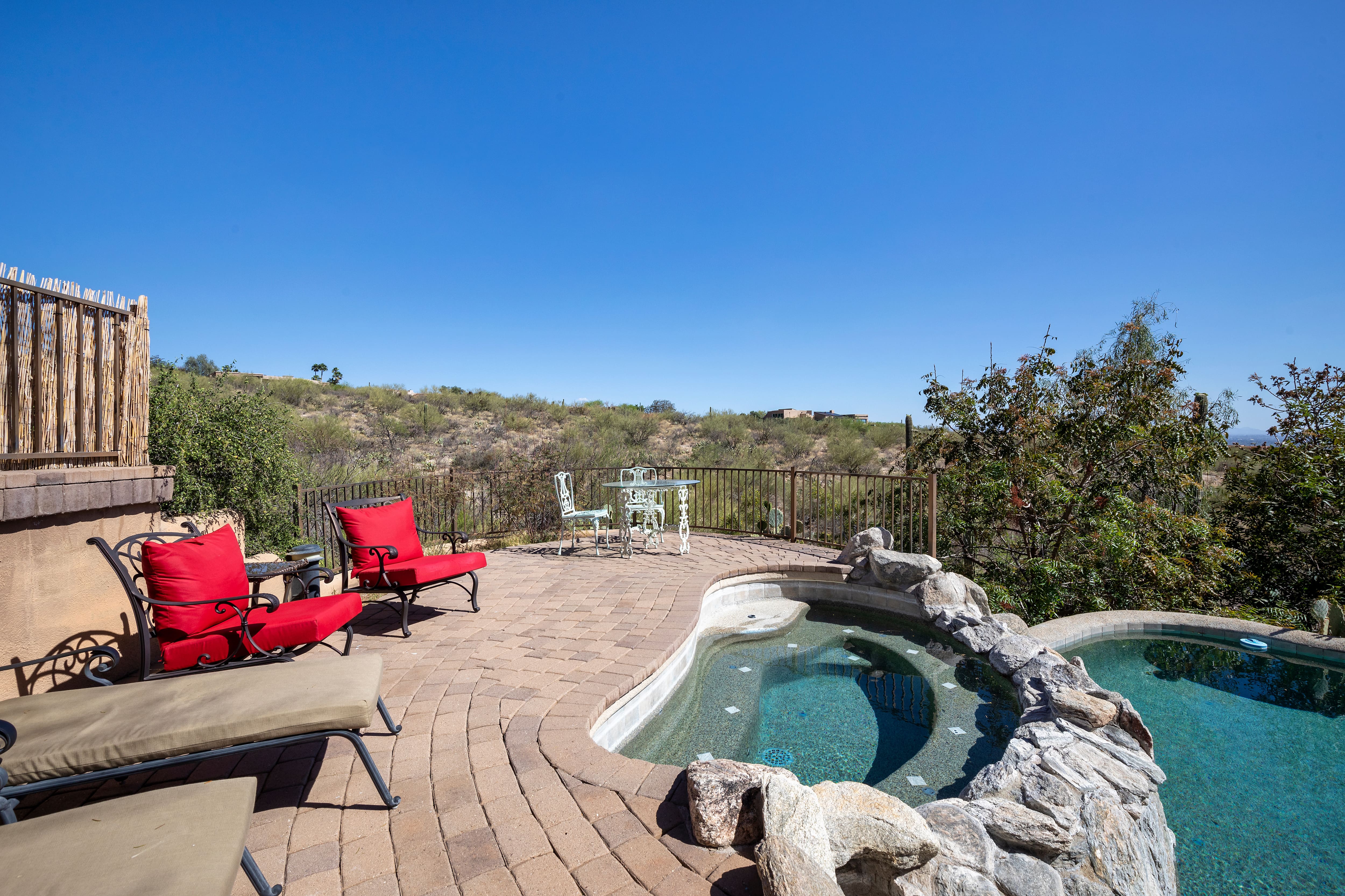 A deck leading down to a patio with a built-in hot tub covered with stone on one side